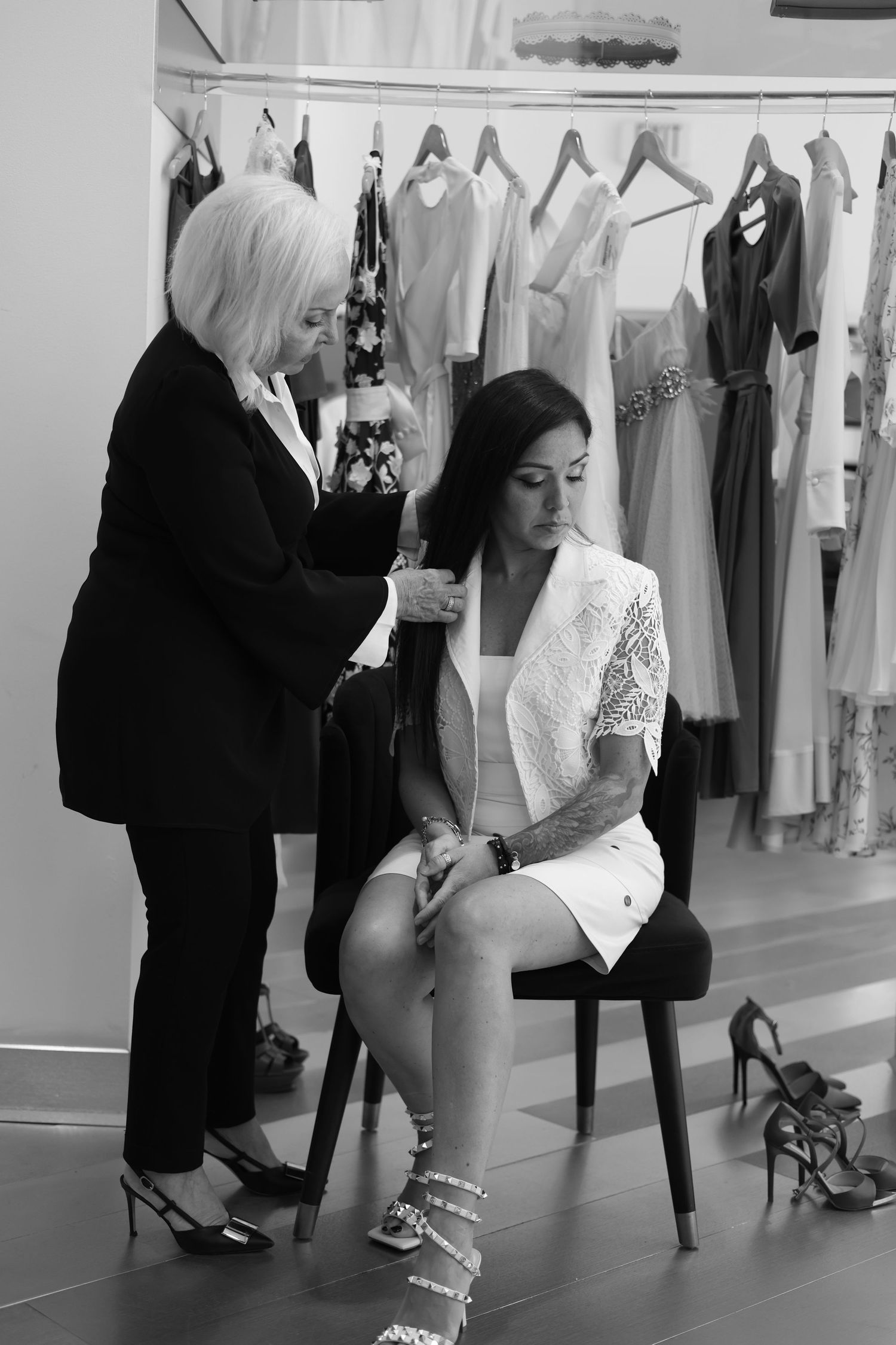 Black and white photo of bridal gown fitting session with seamstress making adjustments in an elegant dress boutique.