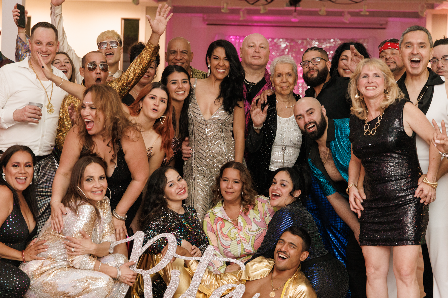 Large diverse group of joyful people posing together at a festive party celebration with gold decorations.