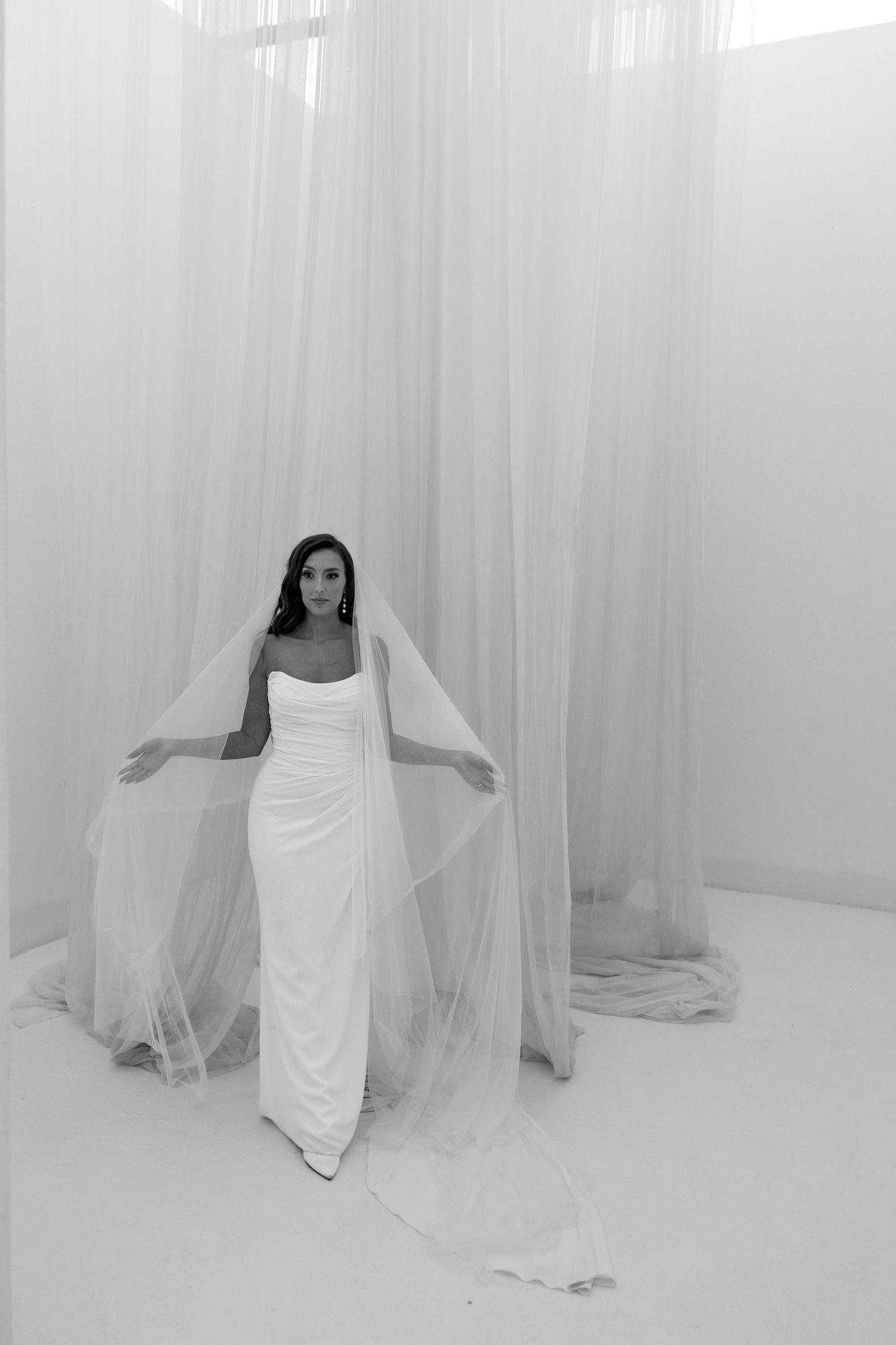 Ethereal white curtains frame a flowing wedding dress in a minimalist setting.