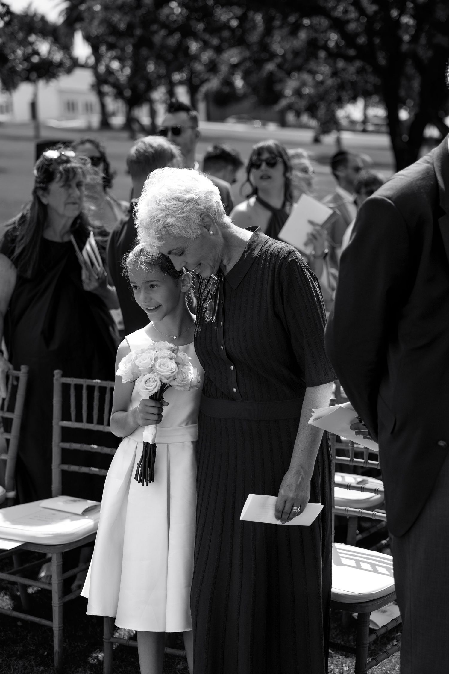 Black and white photograph of a formal outdoor gathering with people in dark suits and white dresses.