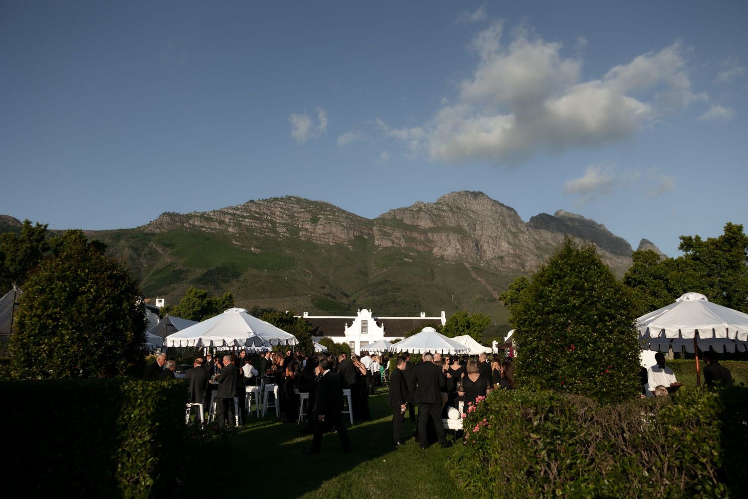 A panoramic view of white wedding tents set up outdoors against a backdrop of mountains and blue sky.