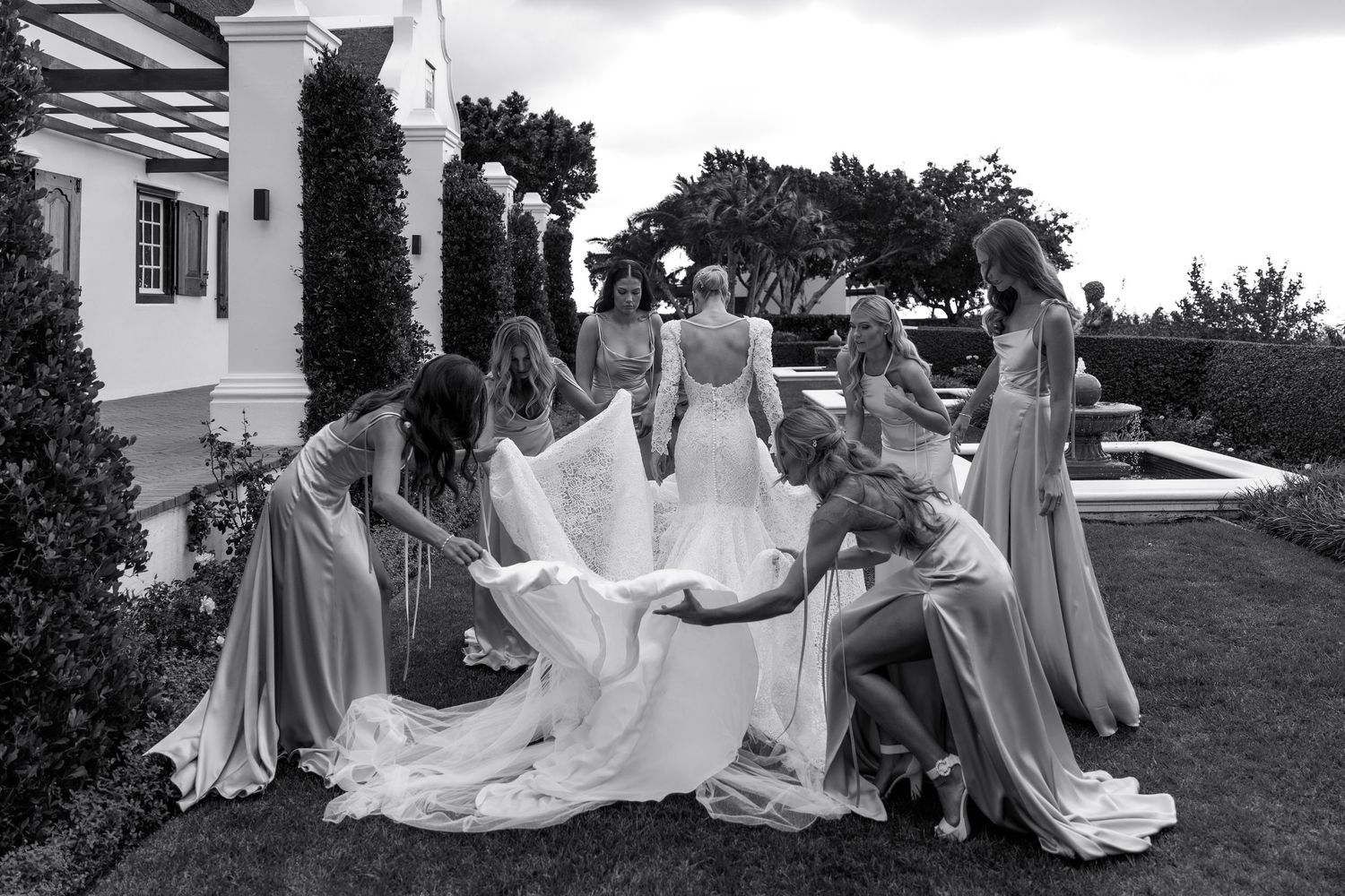 Wedding party members in flowing dresses pose together on a grassy hillside.