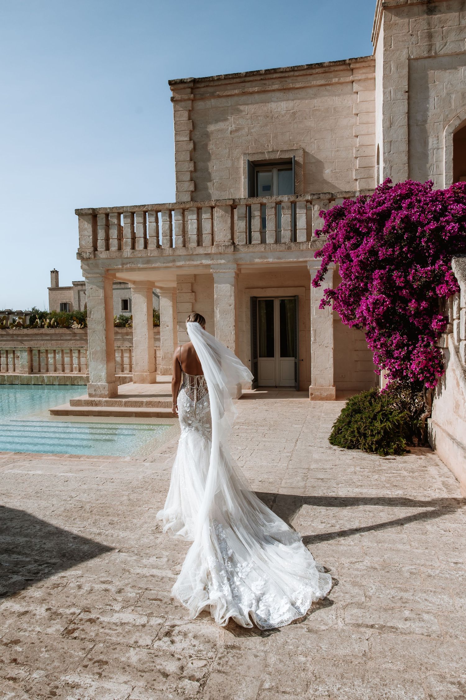 Elegant wedding dress with flowing train photographed at a Mediterranean villa with purple flowers.