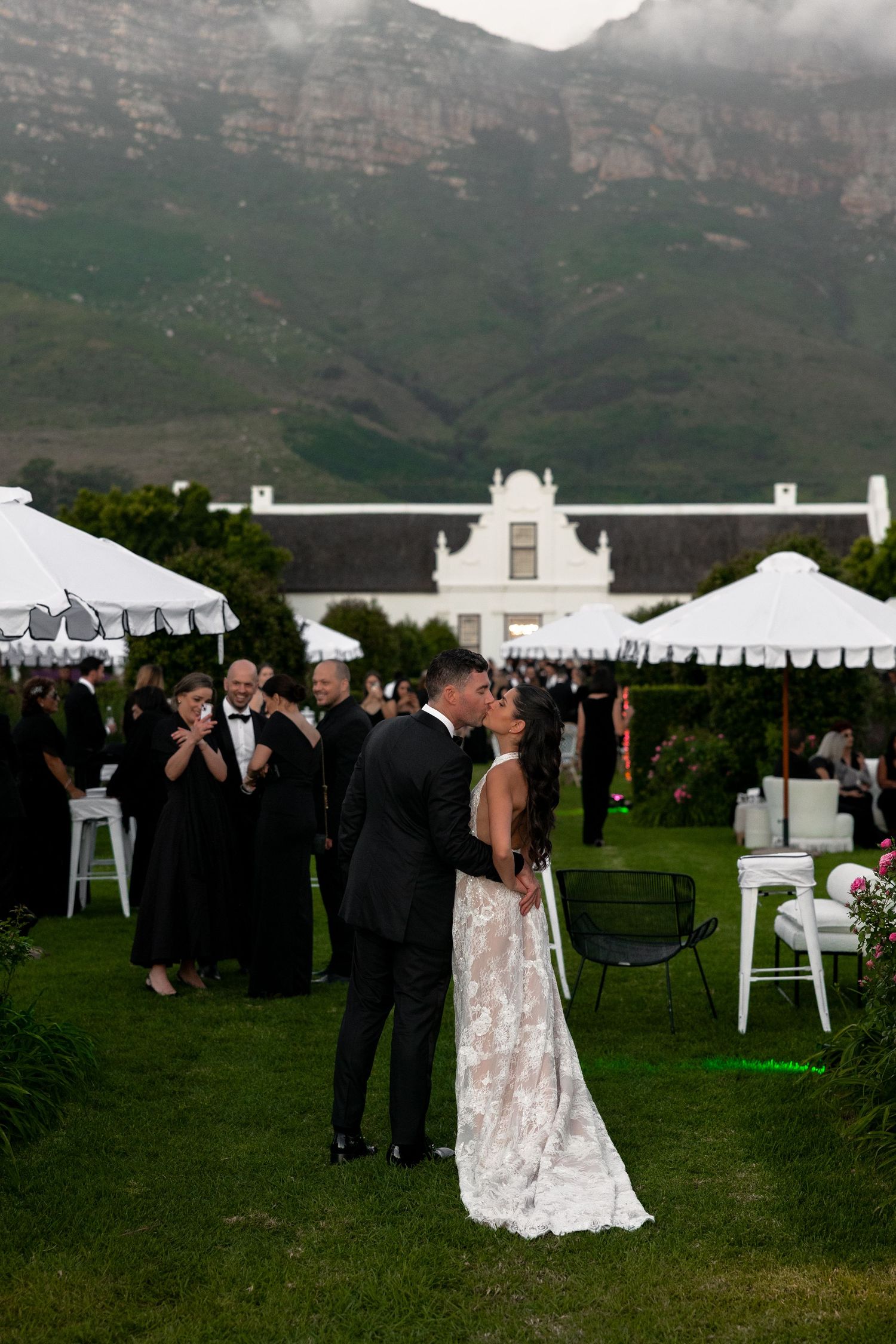 Elegant outdoor wedding reception at a Cape Dutch style venue with mountain backdrop and white tents on manicured lawn.