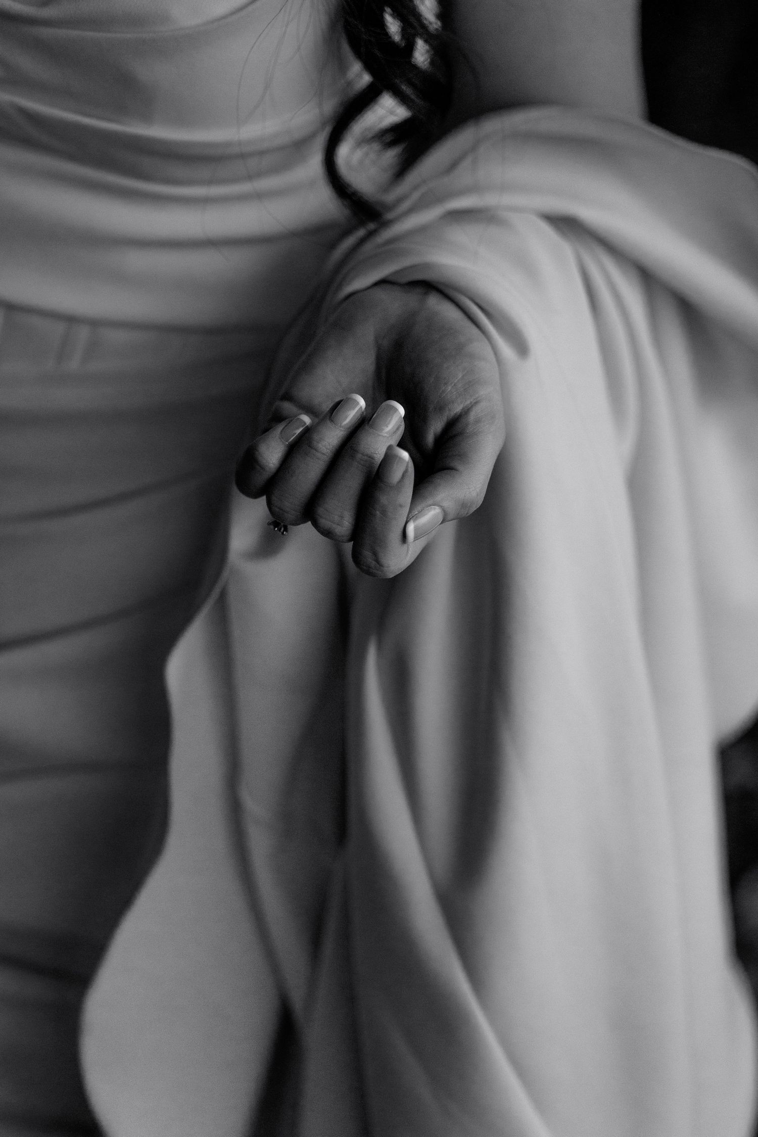 Close-up black and white photo of hands with an engagement ring against flowing white fabric.