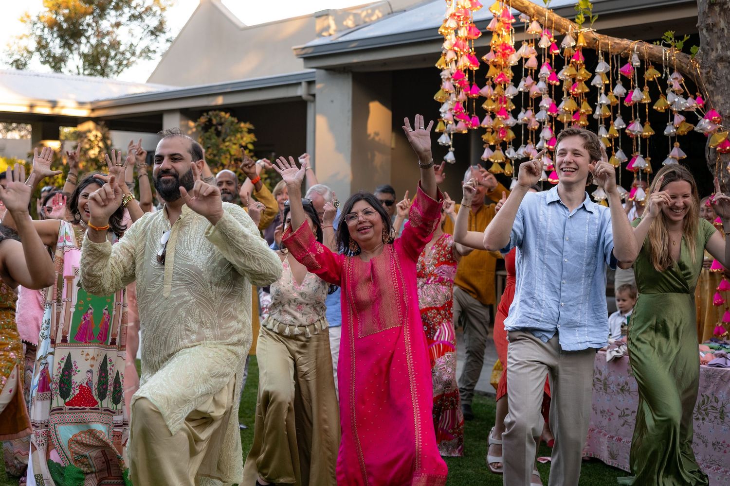 Large group of wedding guests celebrating with colorful decorations overhead.