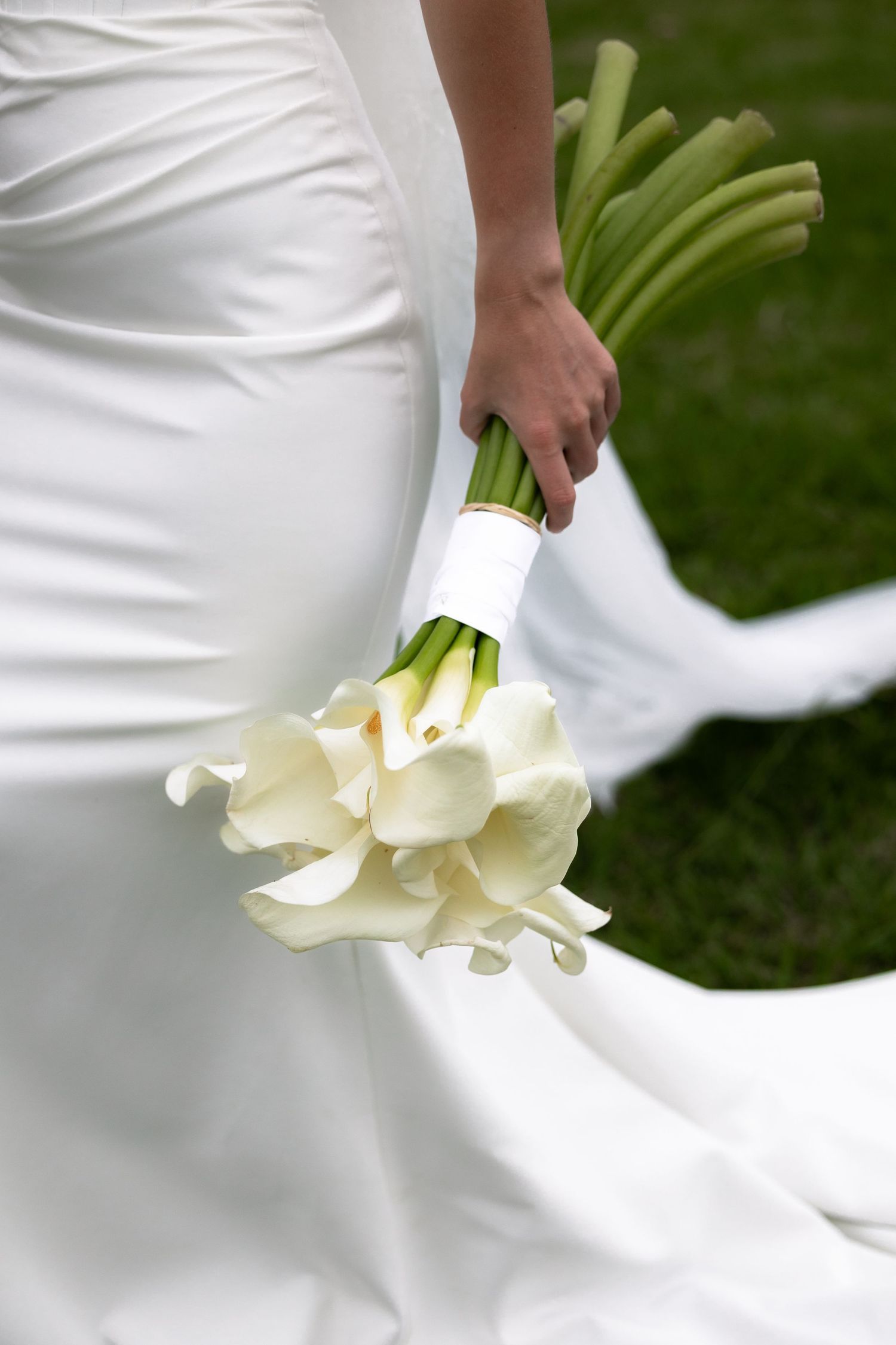 Close-up detail of a flowing white wedding dress train draped elegantly against green grass.