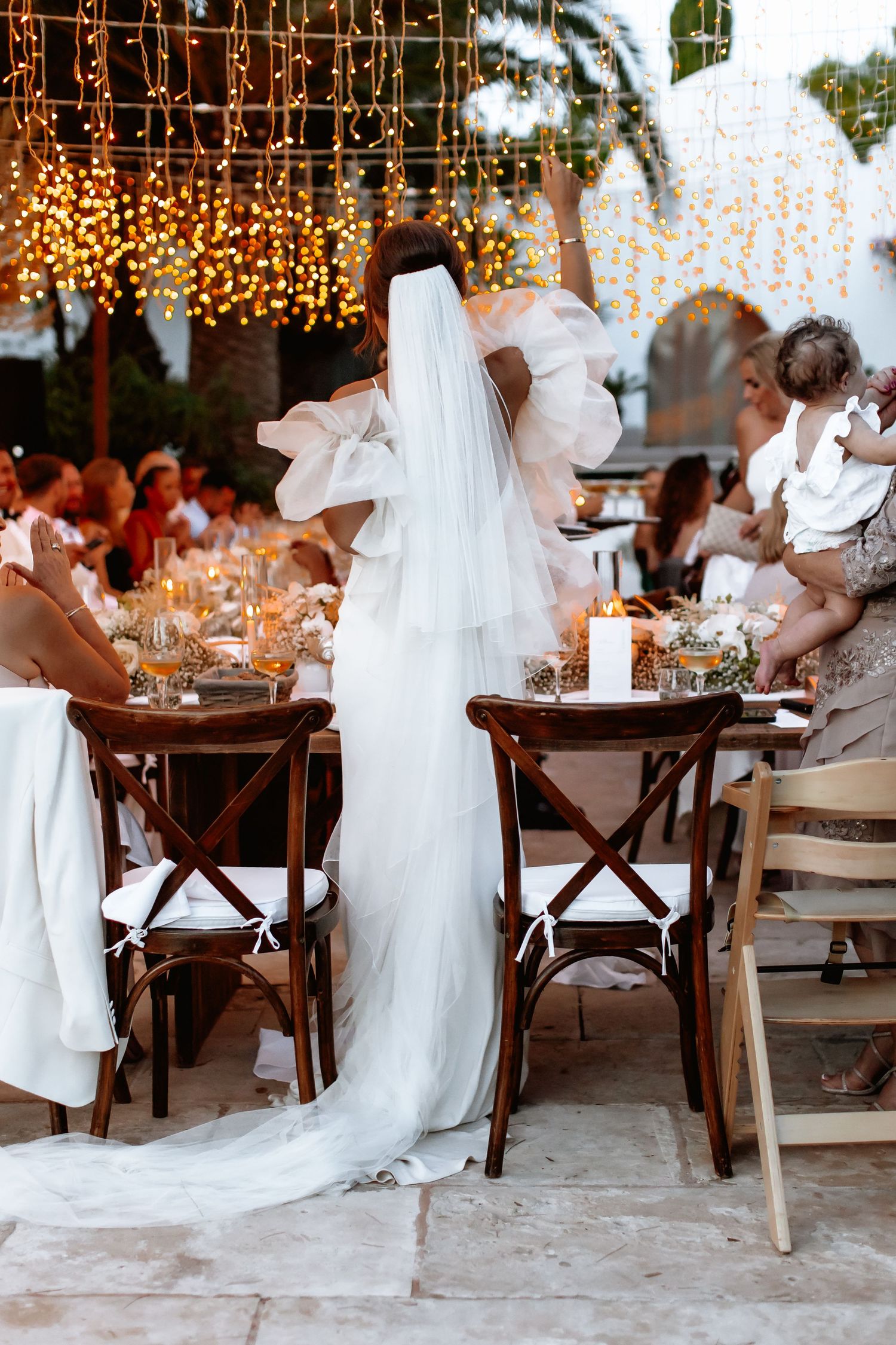 A beach wedding reception setup with wooden tables, white decor, and twinkling lights creating a romantic atmosphere.