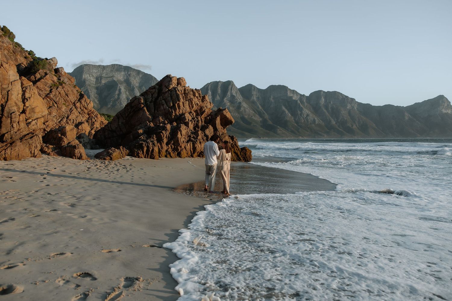 Scenic coastal beach with rugged cliffs and mountains along the shoreline during golden hour.