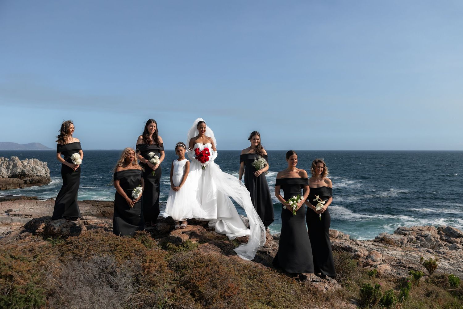 A group of people gather at a scenic coastal cliff overlooking the ocean during a wedding ceremony.