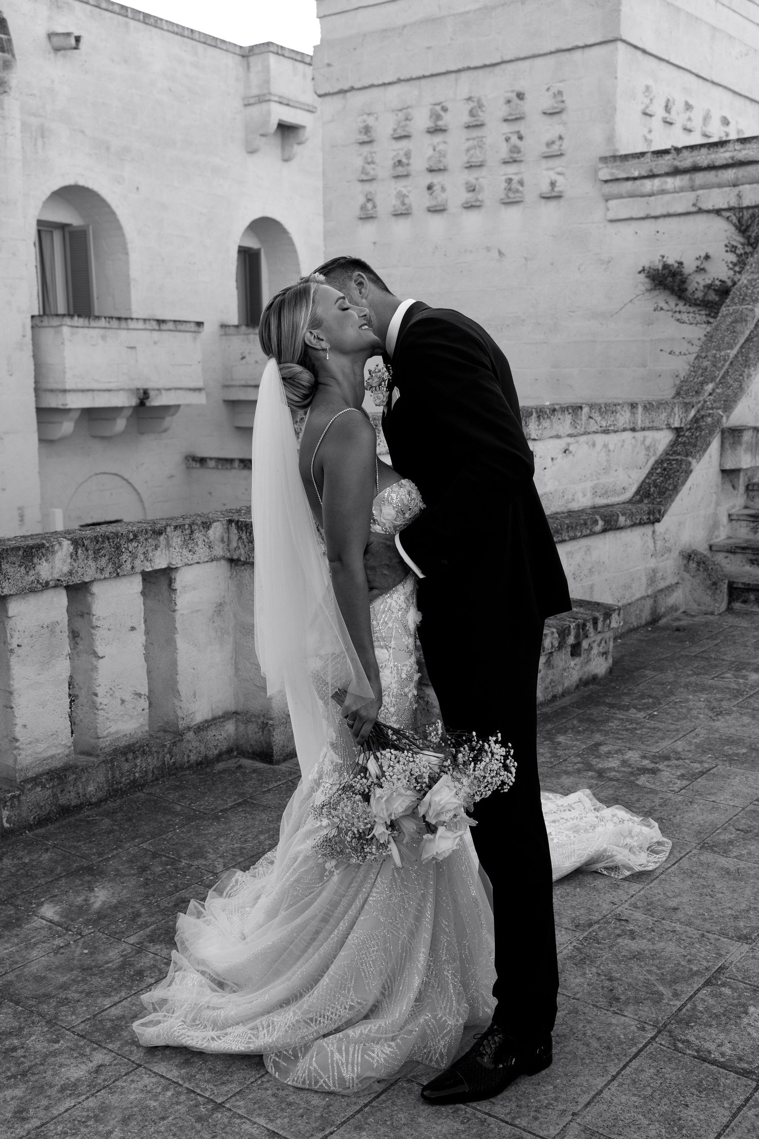 Black and white intimate wedding moment captured against stone architectural backdrop.