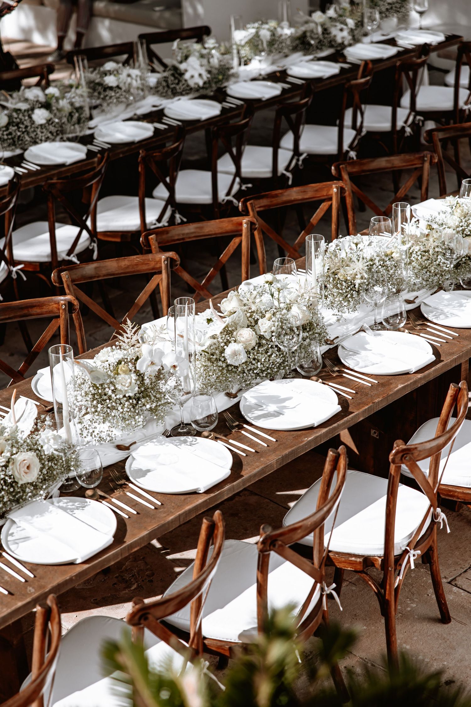 Elegant rustic wedding reception table with dark wood farm tables, white place settings and delicate baby's breath centerpieces.