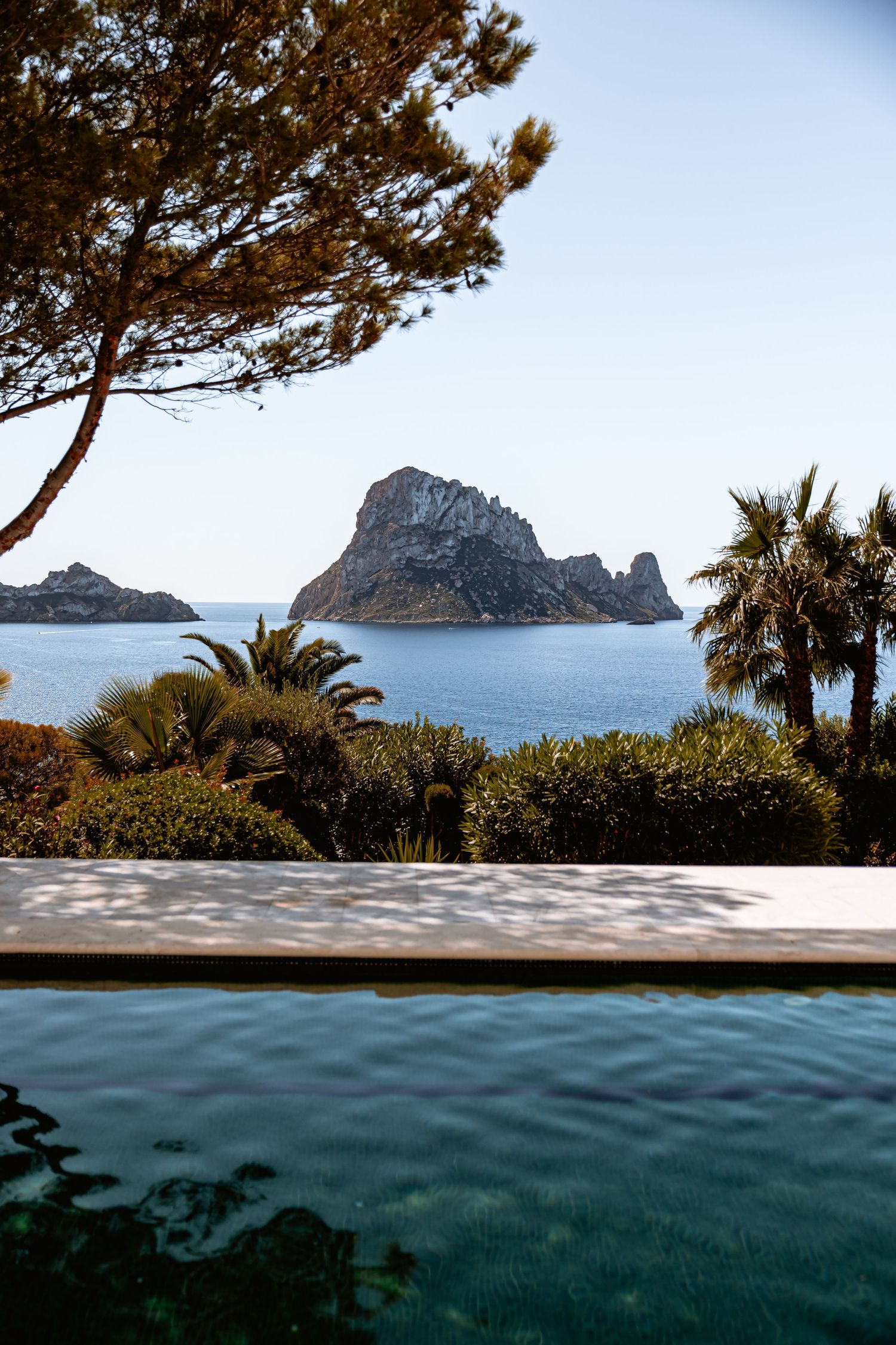 Split view of Mediterranean coastline with rocky islands and palm trees above turquoise waters at Es Vedra, Ibiza.