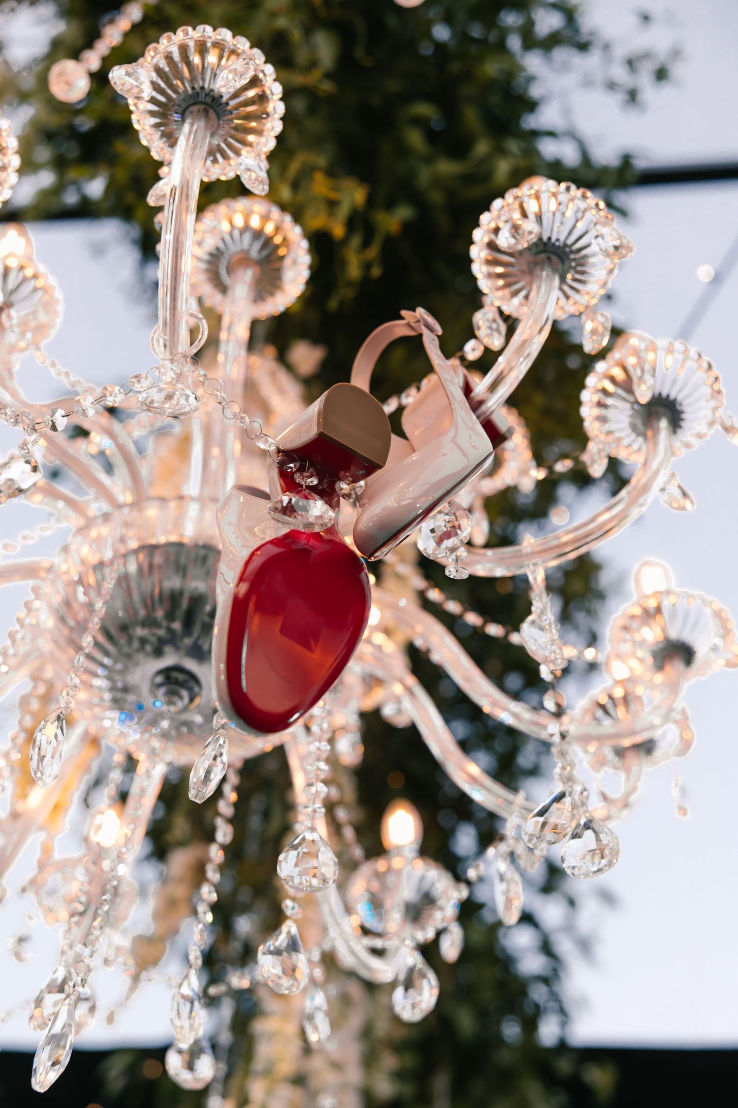Crystal chandelier with red heart ornaments glowing with warm bokeh lights in an elegant holiday display.
