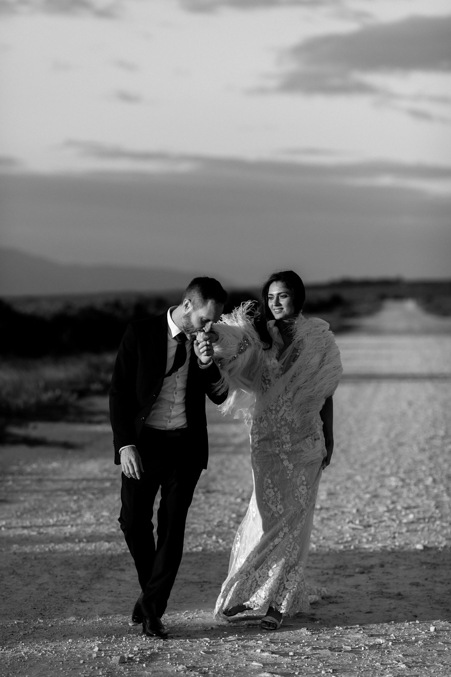 A black and white photo captures a joyful moment on a rocky beach at sunset.
