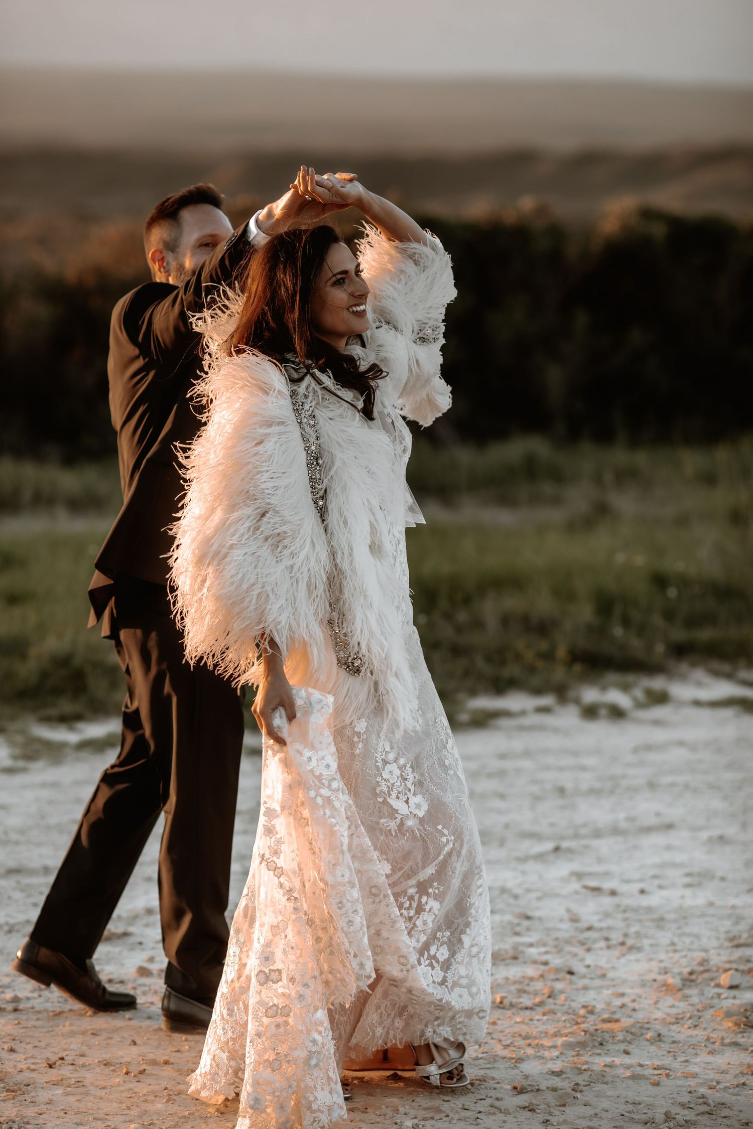 An elegant white lace wedding gown catches the golden light during an outdoor photoshoot.