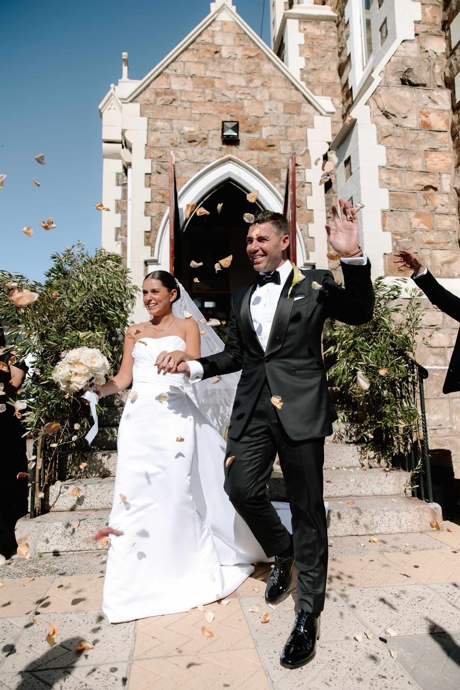 Autumn leaves flutter through the air as a couple celebrates outside a stone church after their wedding ceremony.