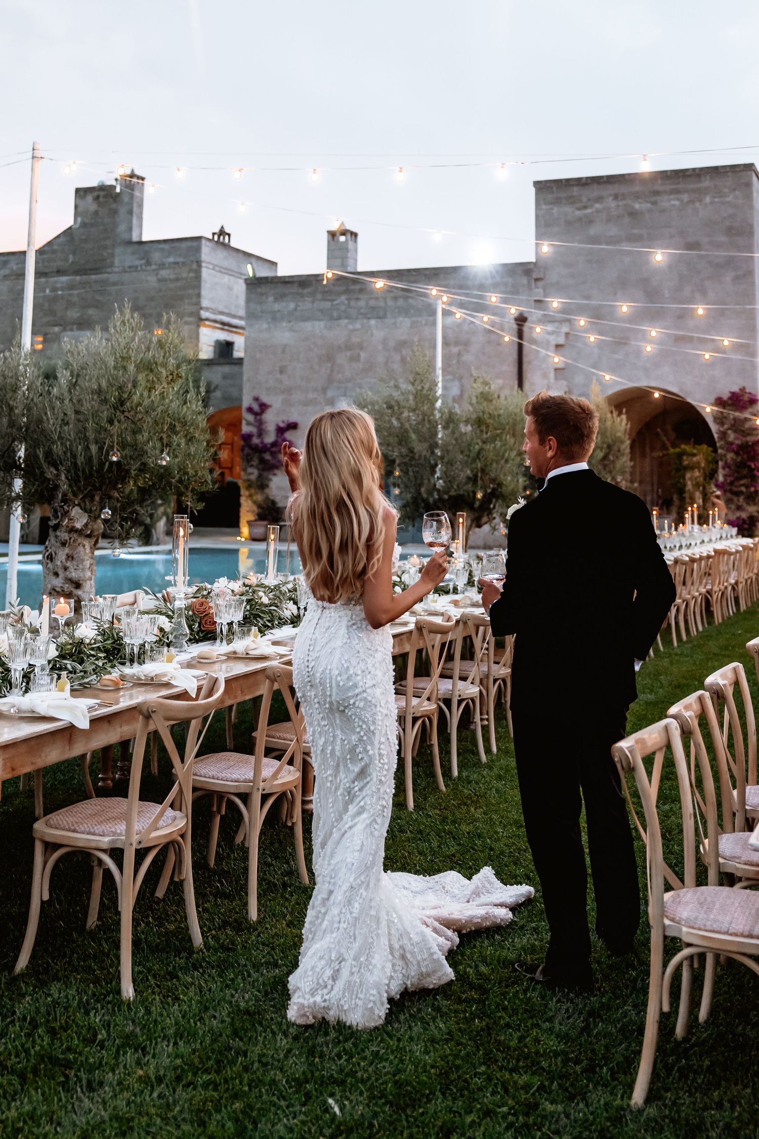 Wedding reception tables set with wooden chairs and string lights in an elegant outdoor setting.