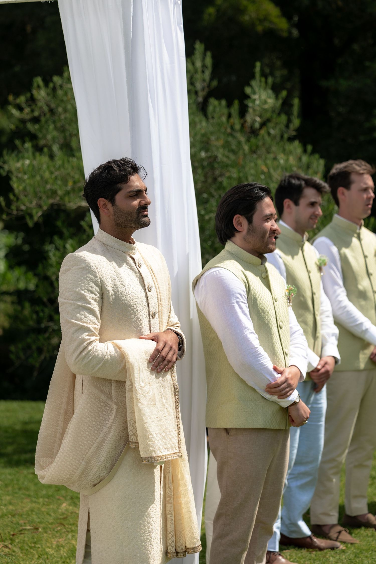 Wedding party members in cream colored formal attire standing in line outdoors.