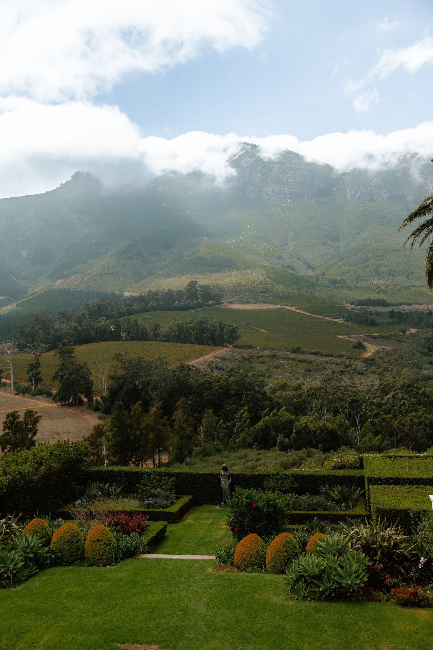 Rolling green hills and mountains create a dramatic landscape vista under cloudy skies in a tropical setting.