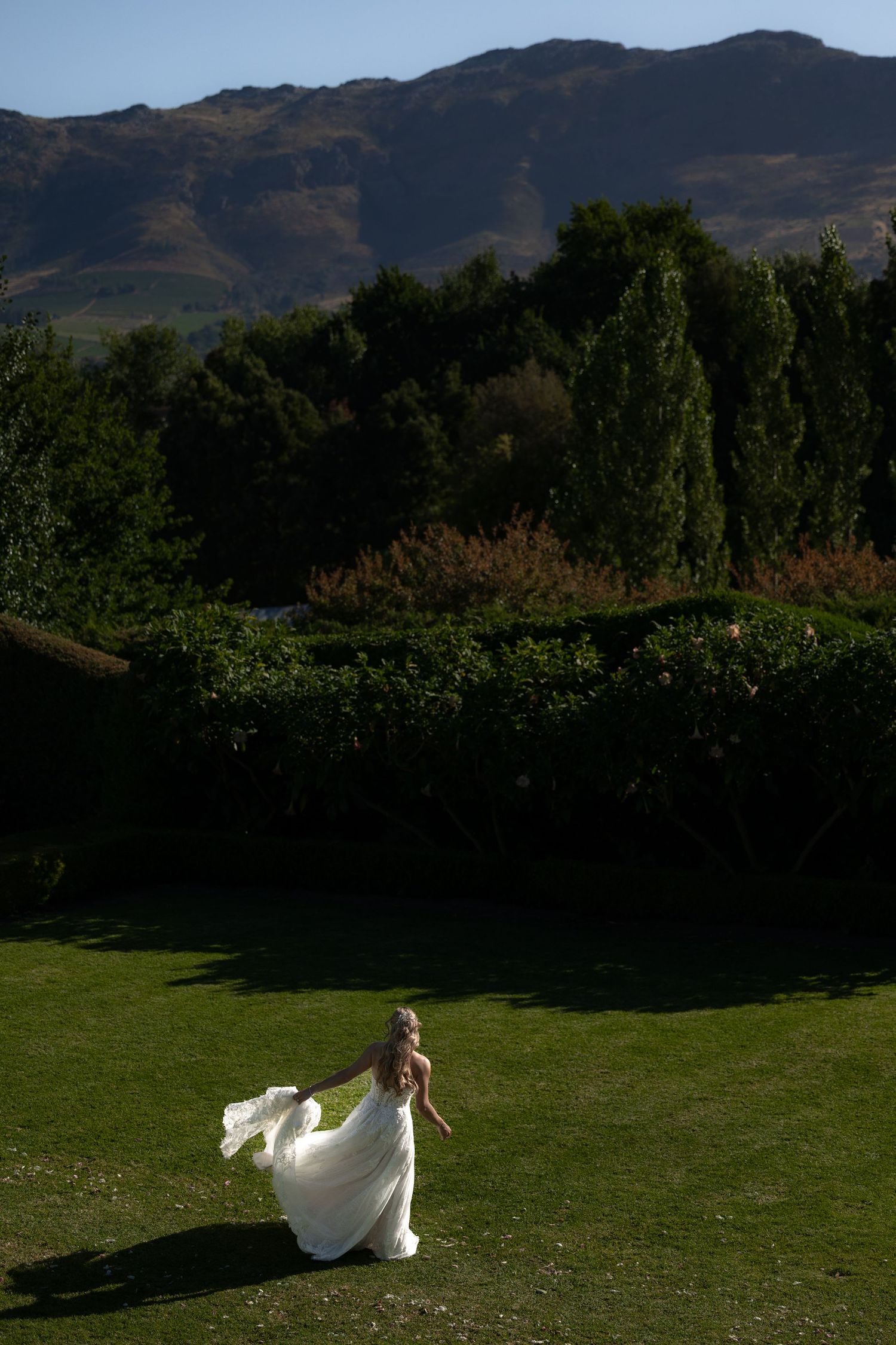 A flowing white dress billows in the wind against a scenic mountain landscape and green meadow backdrop.