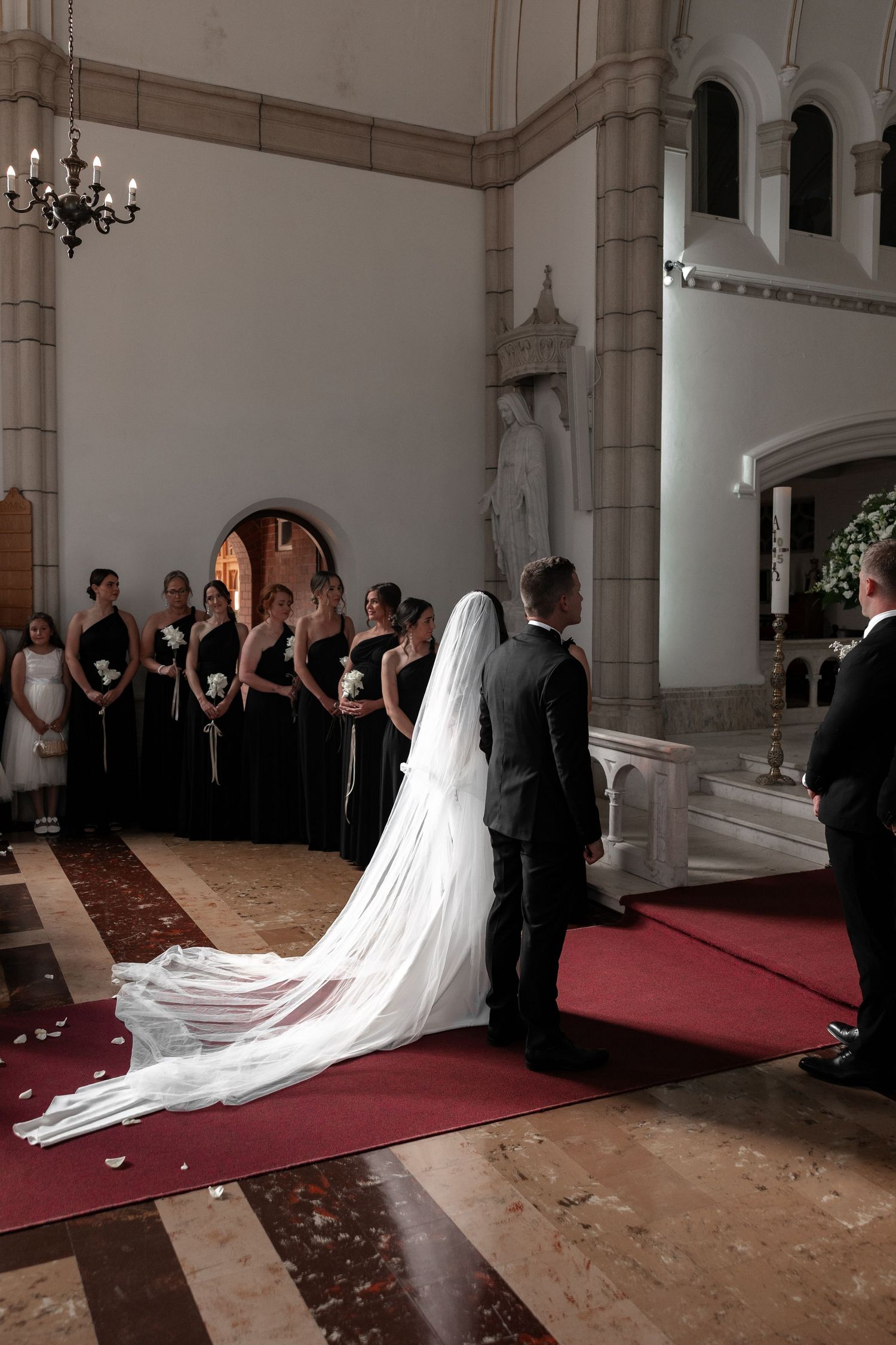 Traditional church wedding ceremony with long flowing bridal veil and red carpet aisle.