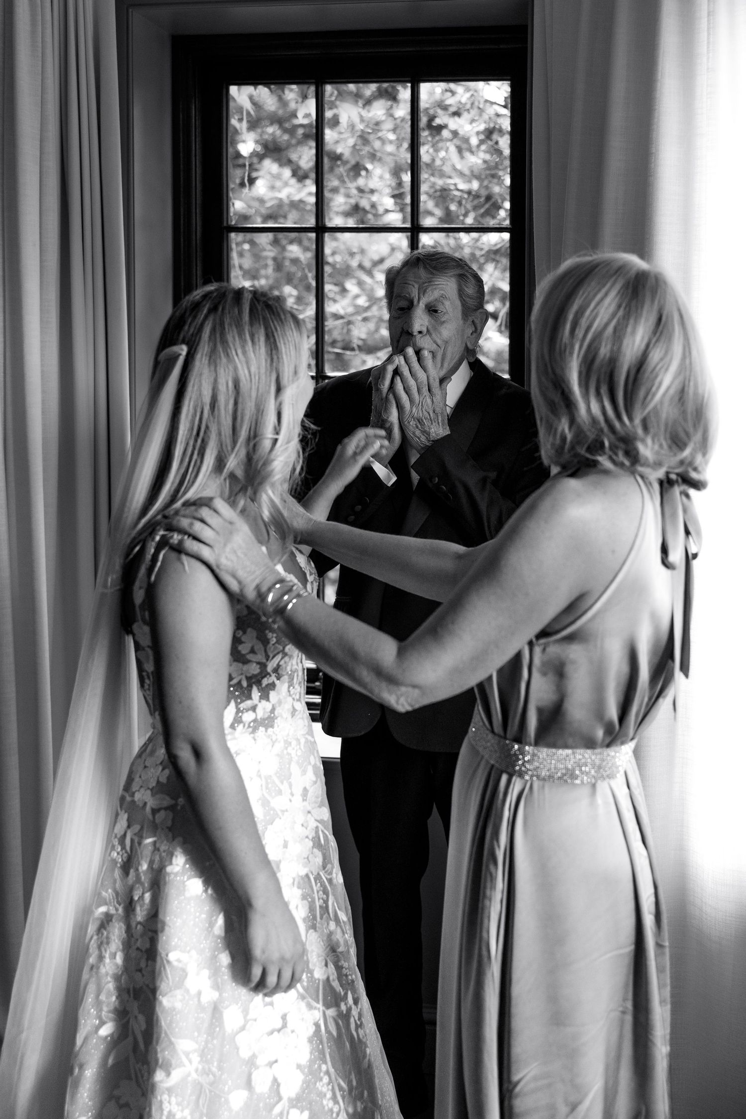 A series of black and white photos showing bridesmaids helping each other get ready by a bright window.