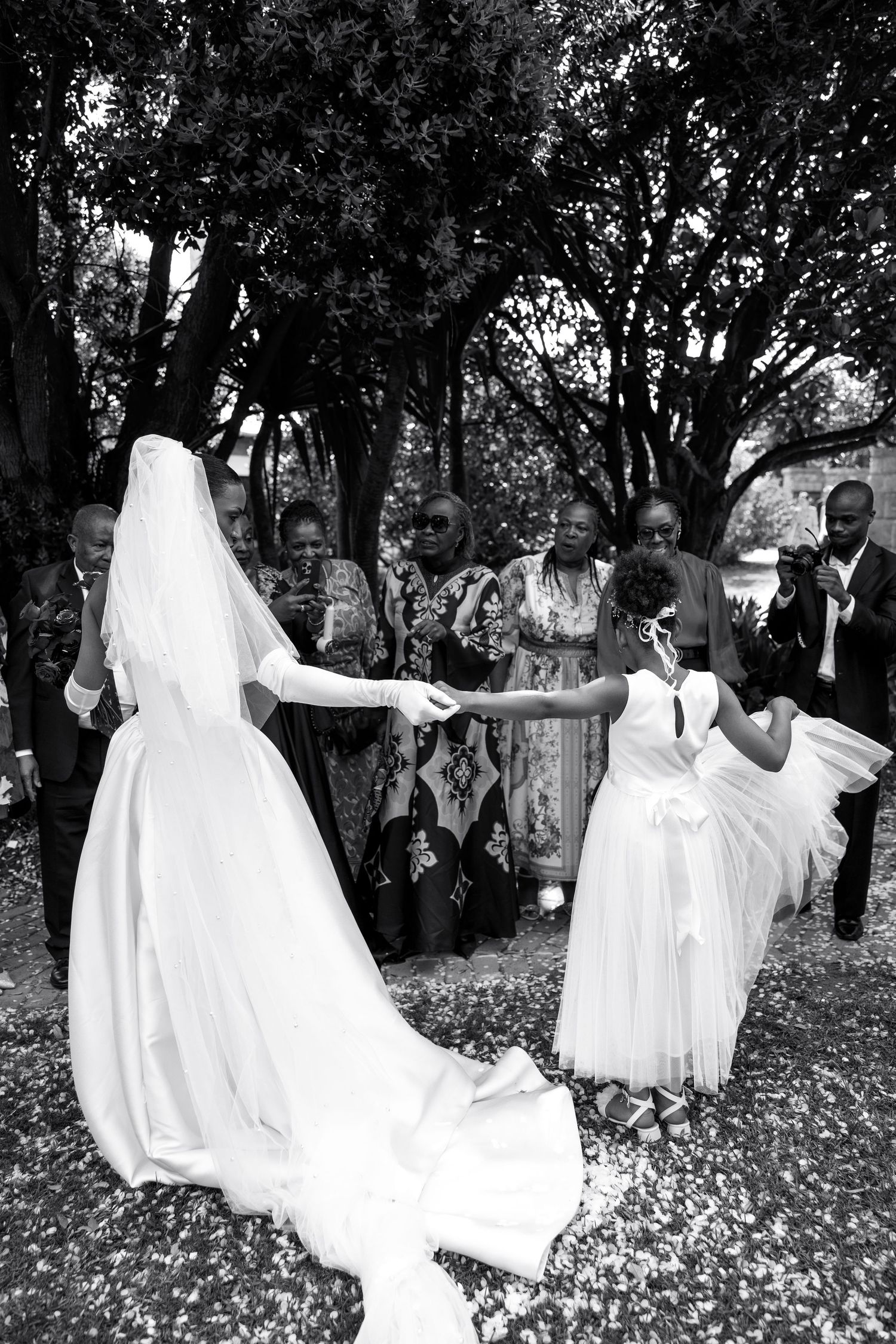 Joyful wedding celebration in a garden setting with flowing white dresses and natural scenery.