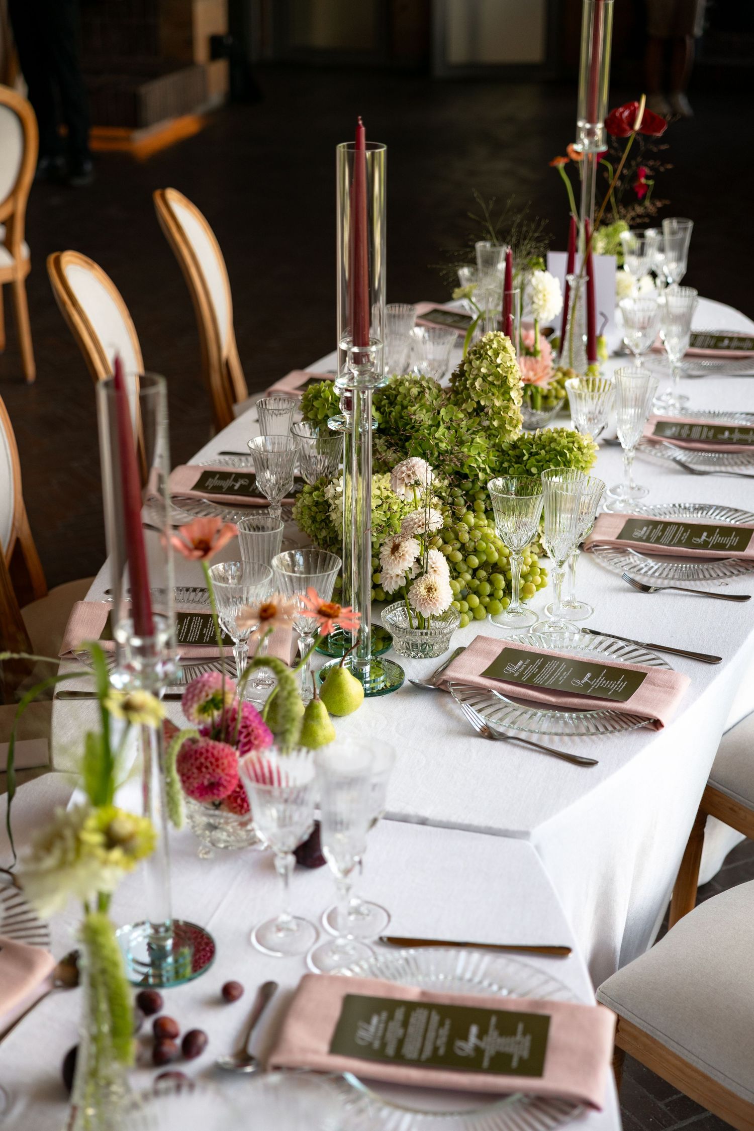 Elegant wedding reception table settings with white linens, glass vases, greenery and chalkboard menus at each place setting.