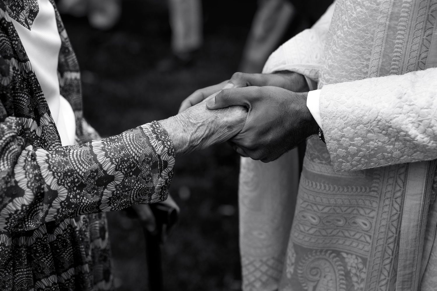 Black and white photo of two people holding hands with intricate henna designs during a wedding ceremony.