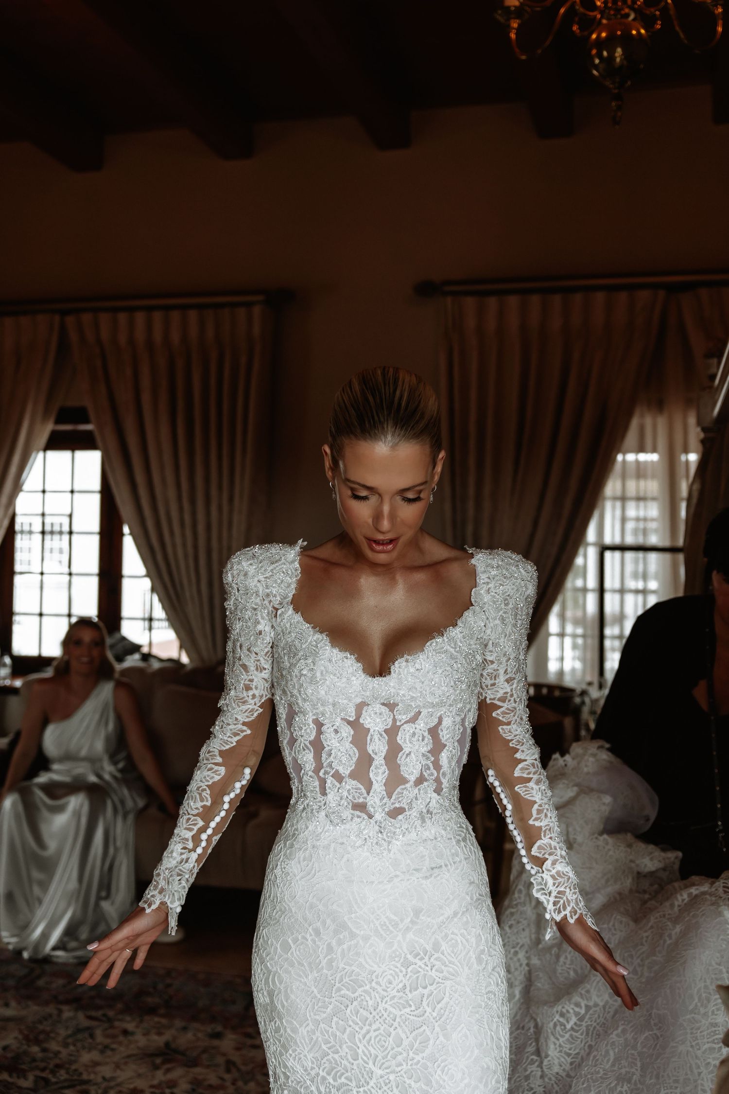 Elegant lace wedding dress with long sleeves and intricate sheer bodice details in a romantic indoor setting.