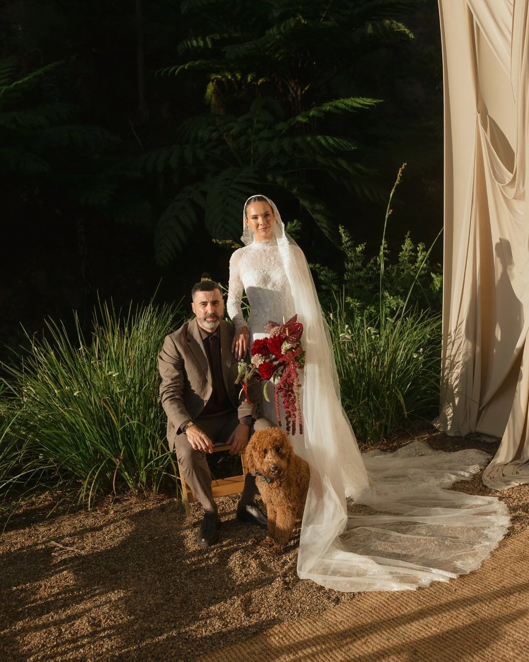 A couple poses with their dog during a wedding photo session outdoors at dusk.