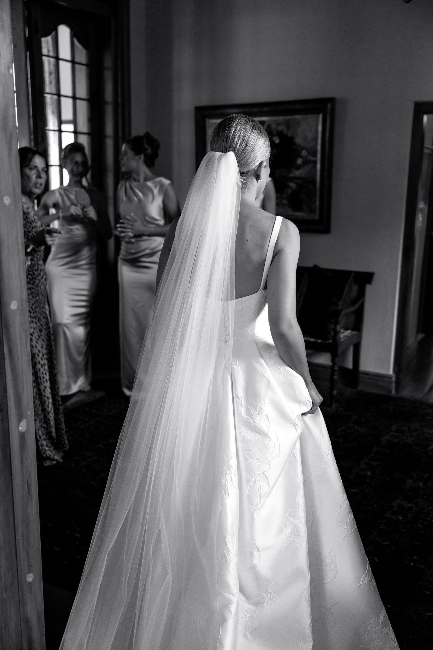 Black and white photo showing a flowing white wedding dress and veil in a room with mirrors.