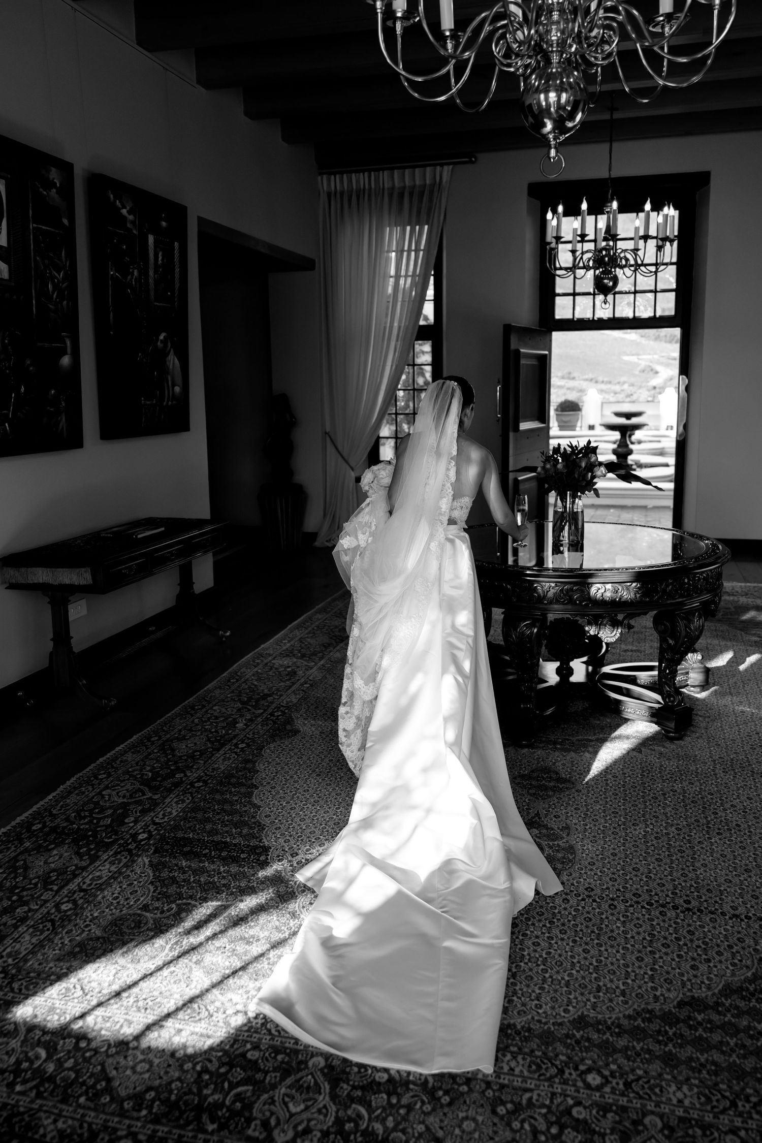 A flowing white wedding gown photographed in dramatic black and white with sunlight streaming through windows.