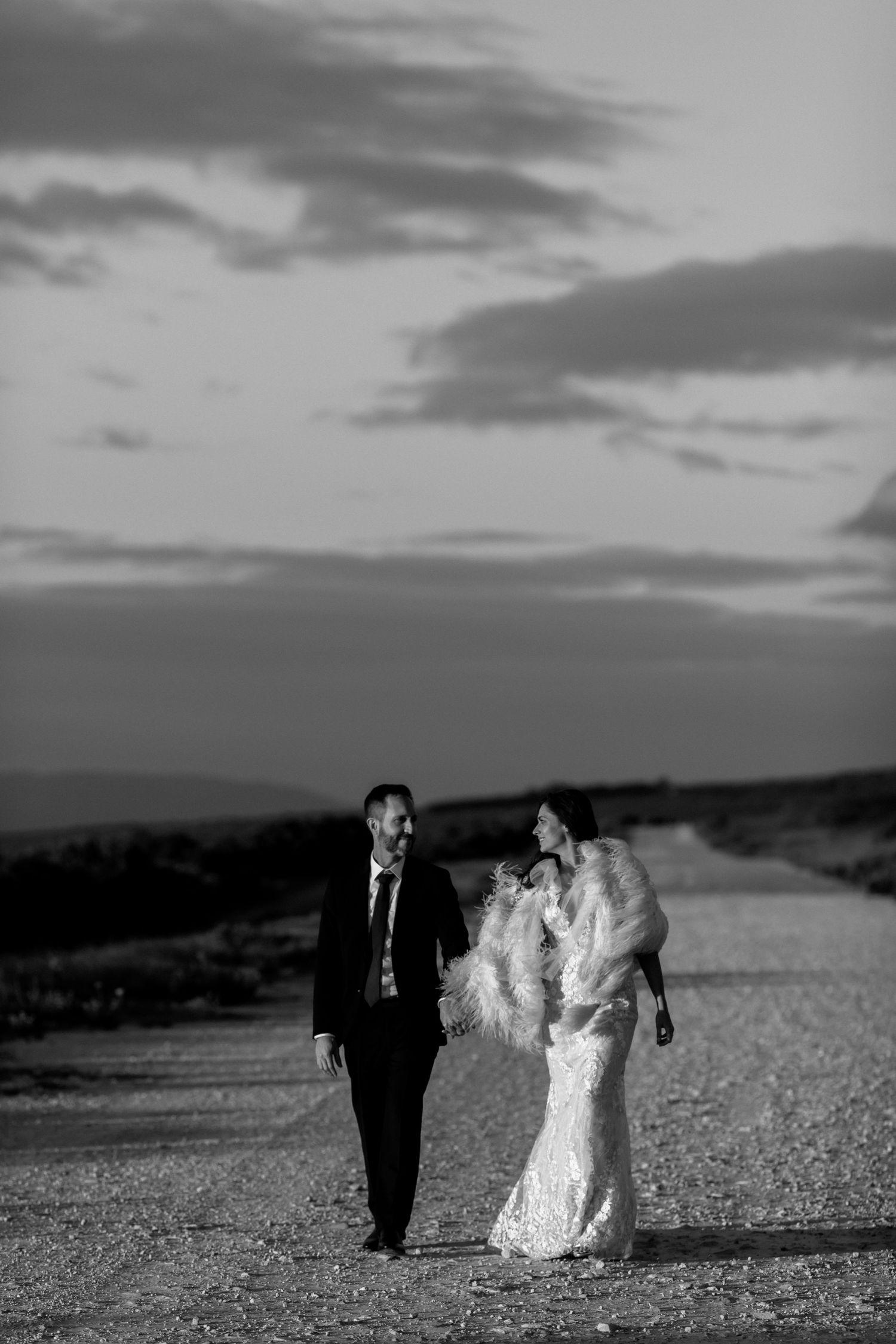 Silhouettes walk across a dramatic landscape in formal wedding attire during sunset.