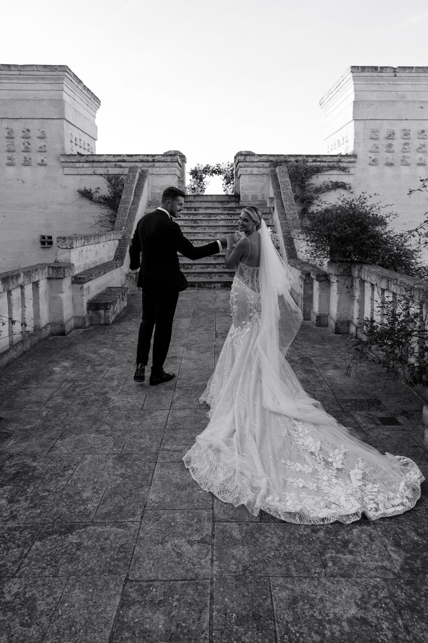 Black and white photo of couple dancing on stone terrace with bride's dress flowing.