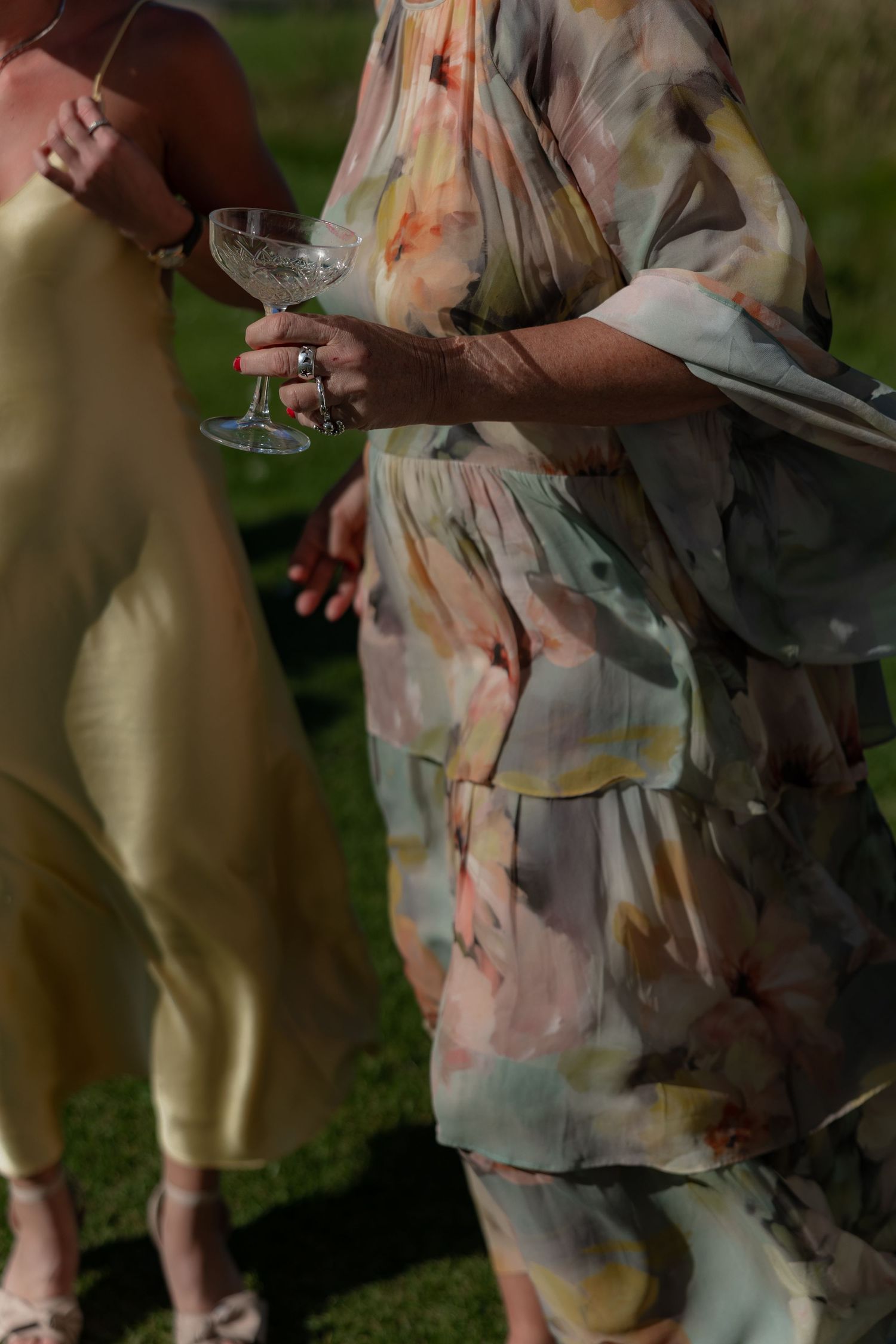 People in floral dresses gather outdoors on grass during a social event or celebration.