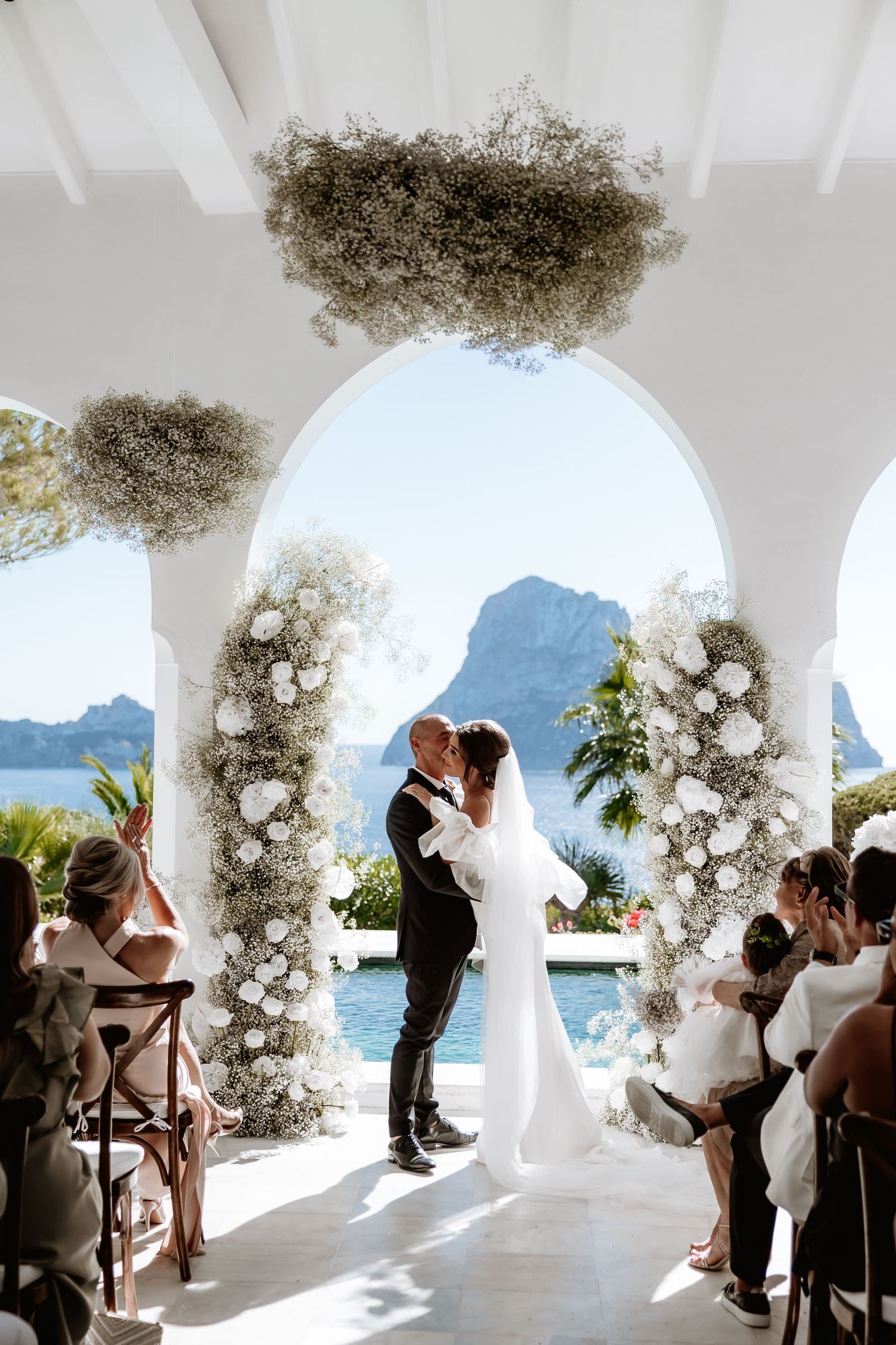 A romantic wedding ceremony takes place under a floral arch overlooking a stunning mountain lake view.