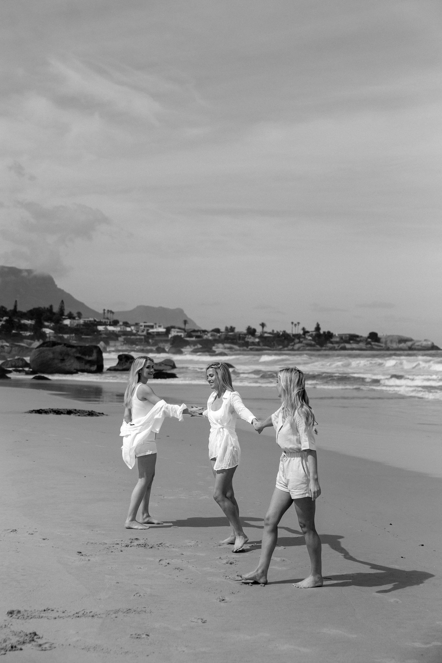Black and white photo of three people walking along a coastal beach.