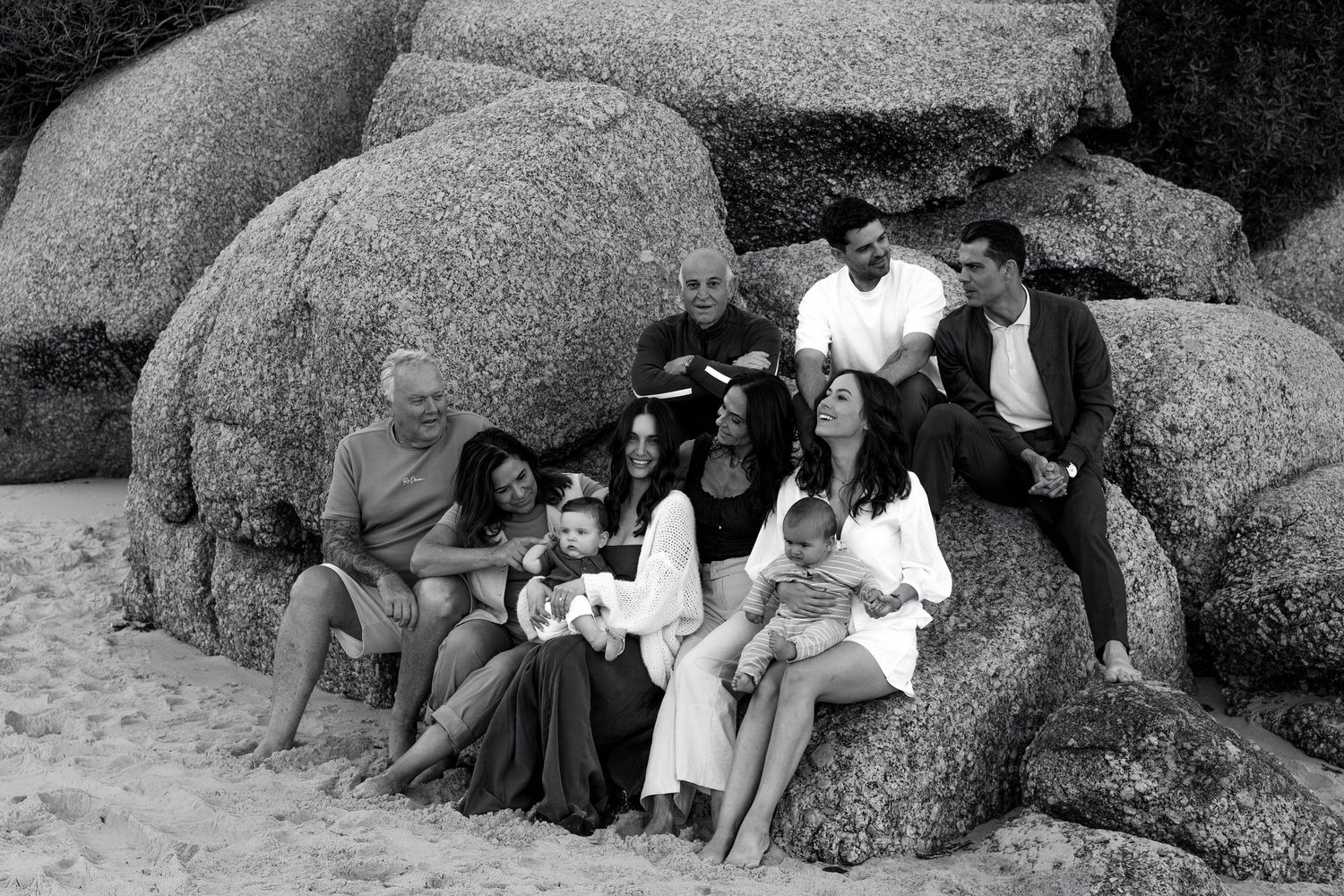 Black and white photo of a large family group posing together on sandy beach rocks, spanning multiple generations.