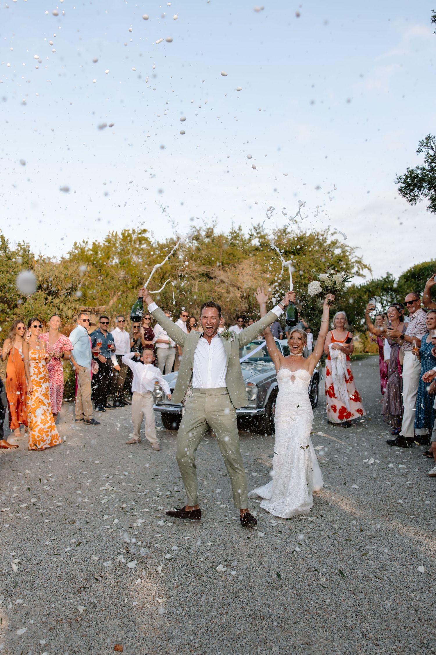 Wedding guests toss flower petals in celebration as the newlyweds walk through on a beach path.