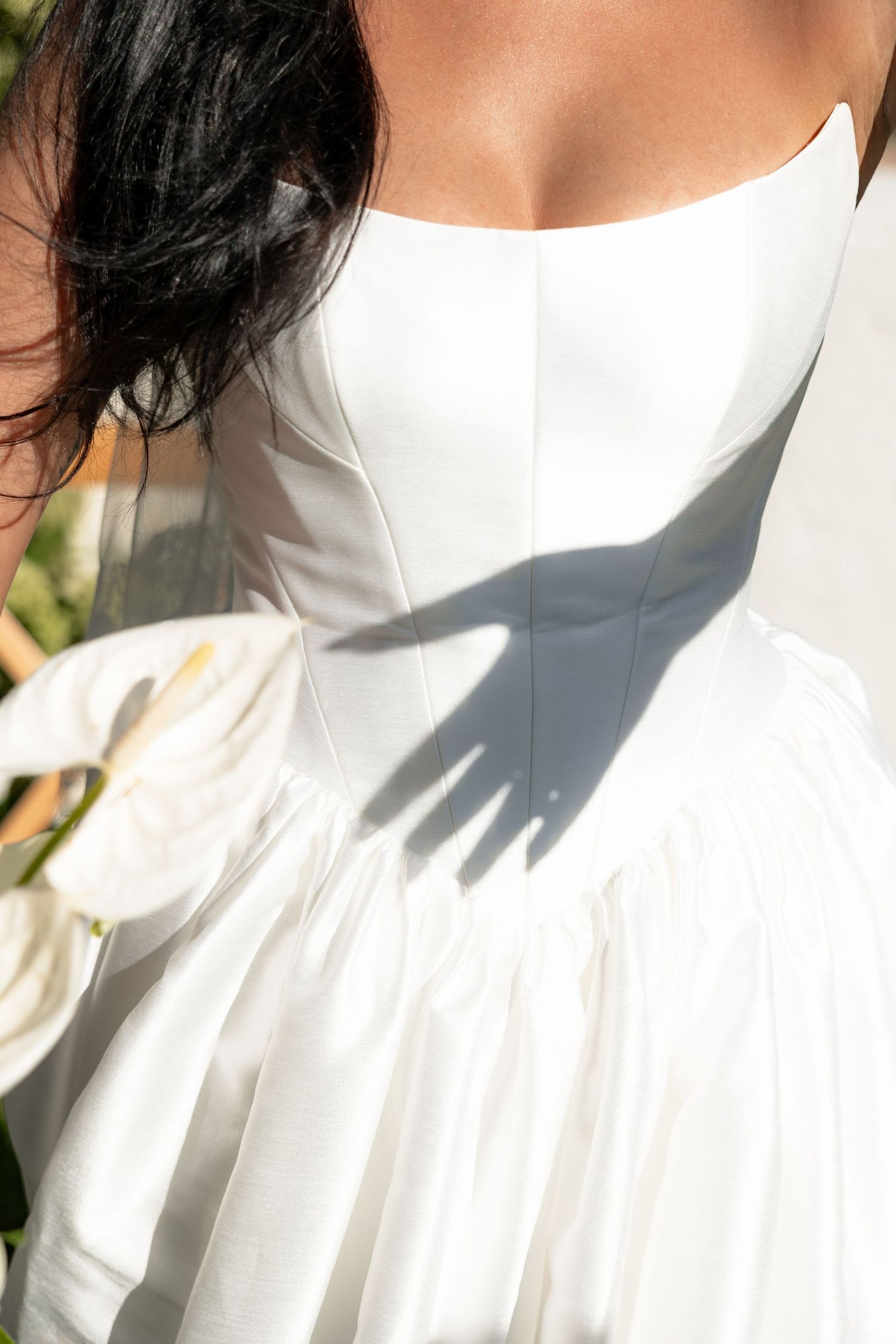 Close-up view of a white wedding dress fabric with delicate pleating details in natural lighting.