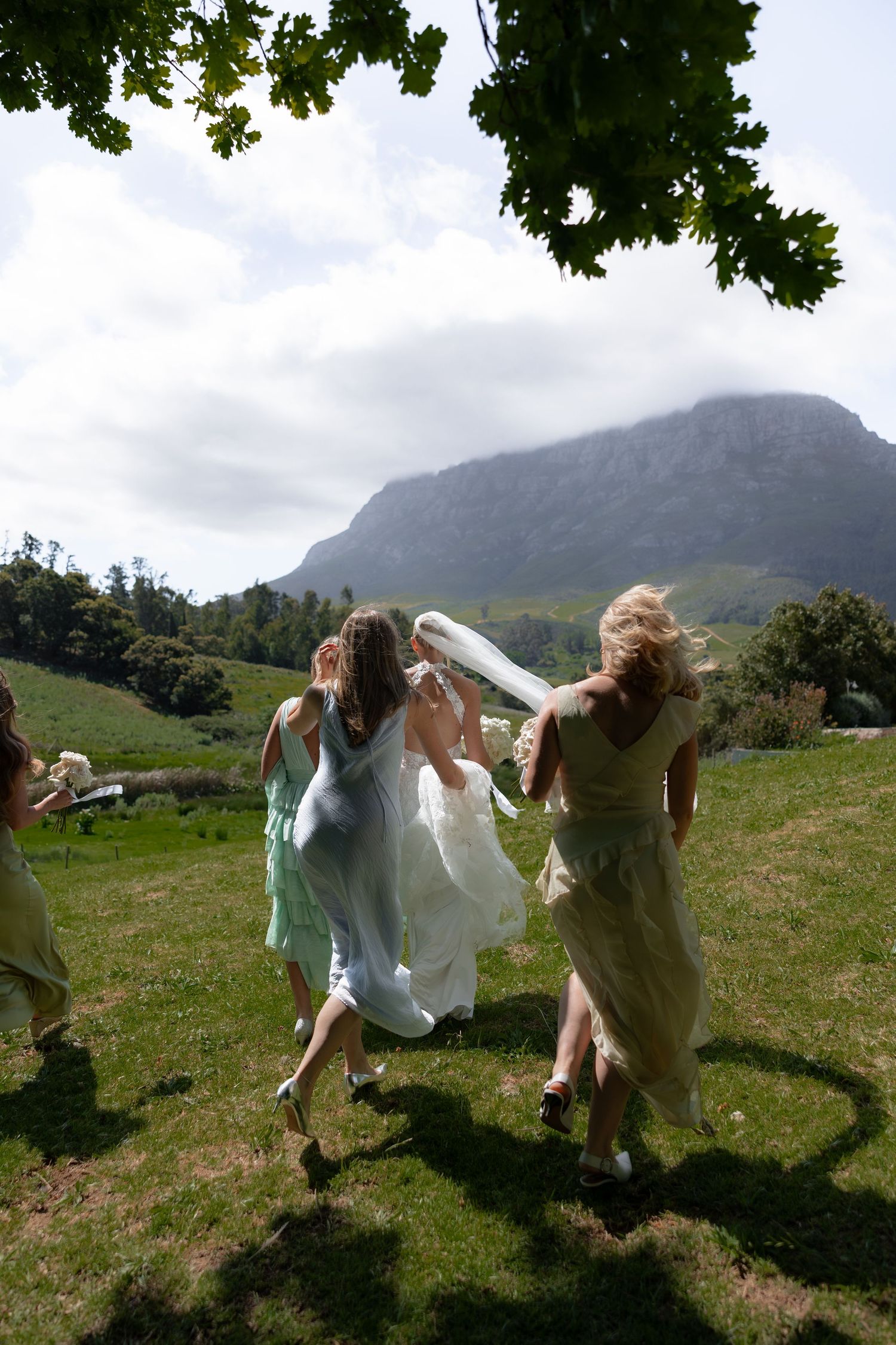 A sequence of people dancing and spinning in a green field with mountains in the background on a cloudy day.