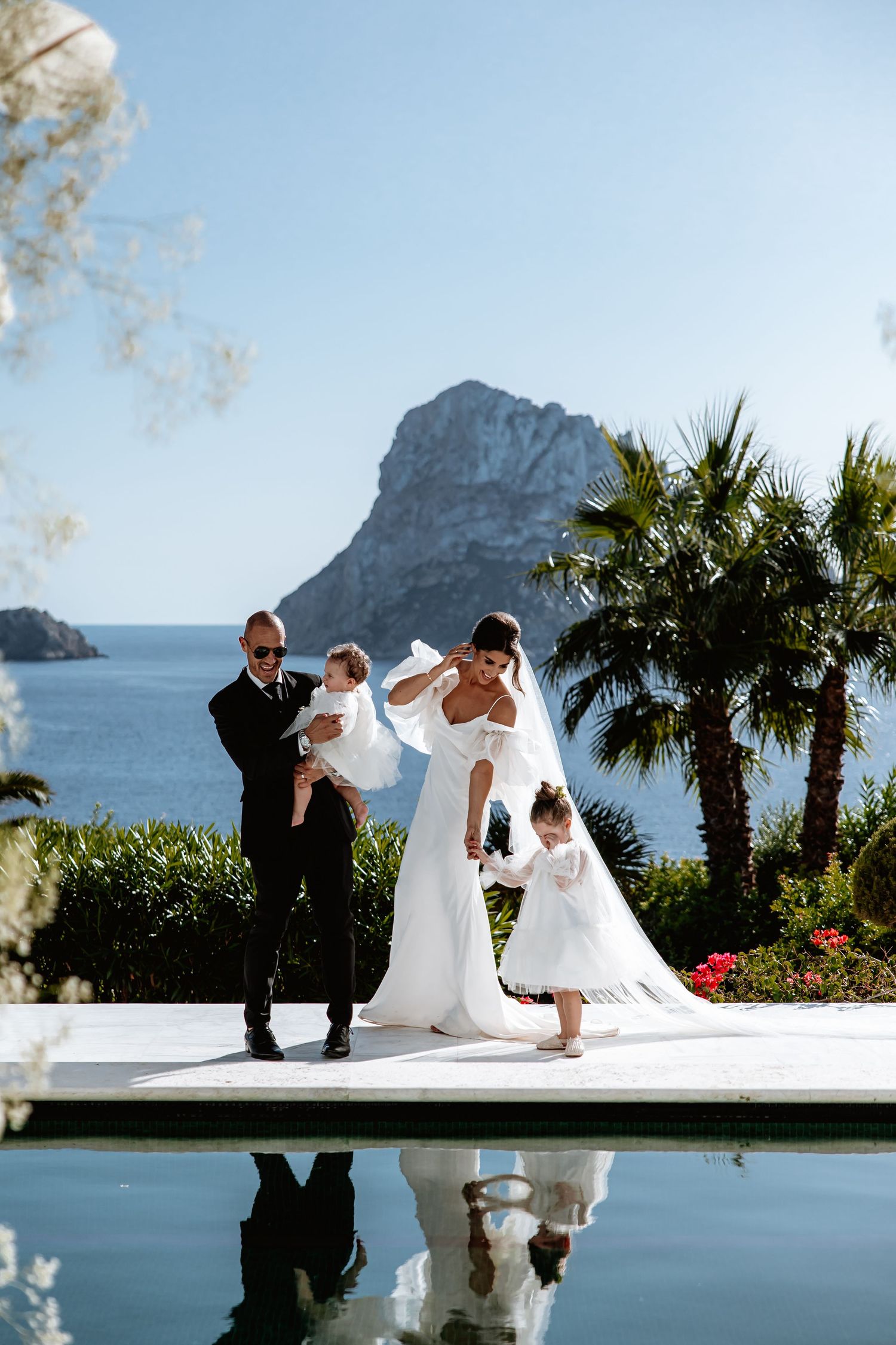 Wedding party poses for creative reflection photos with mountain and ocean backdrop in Mediterranean setting.