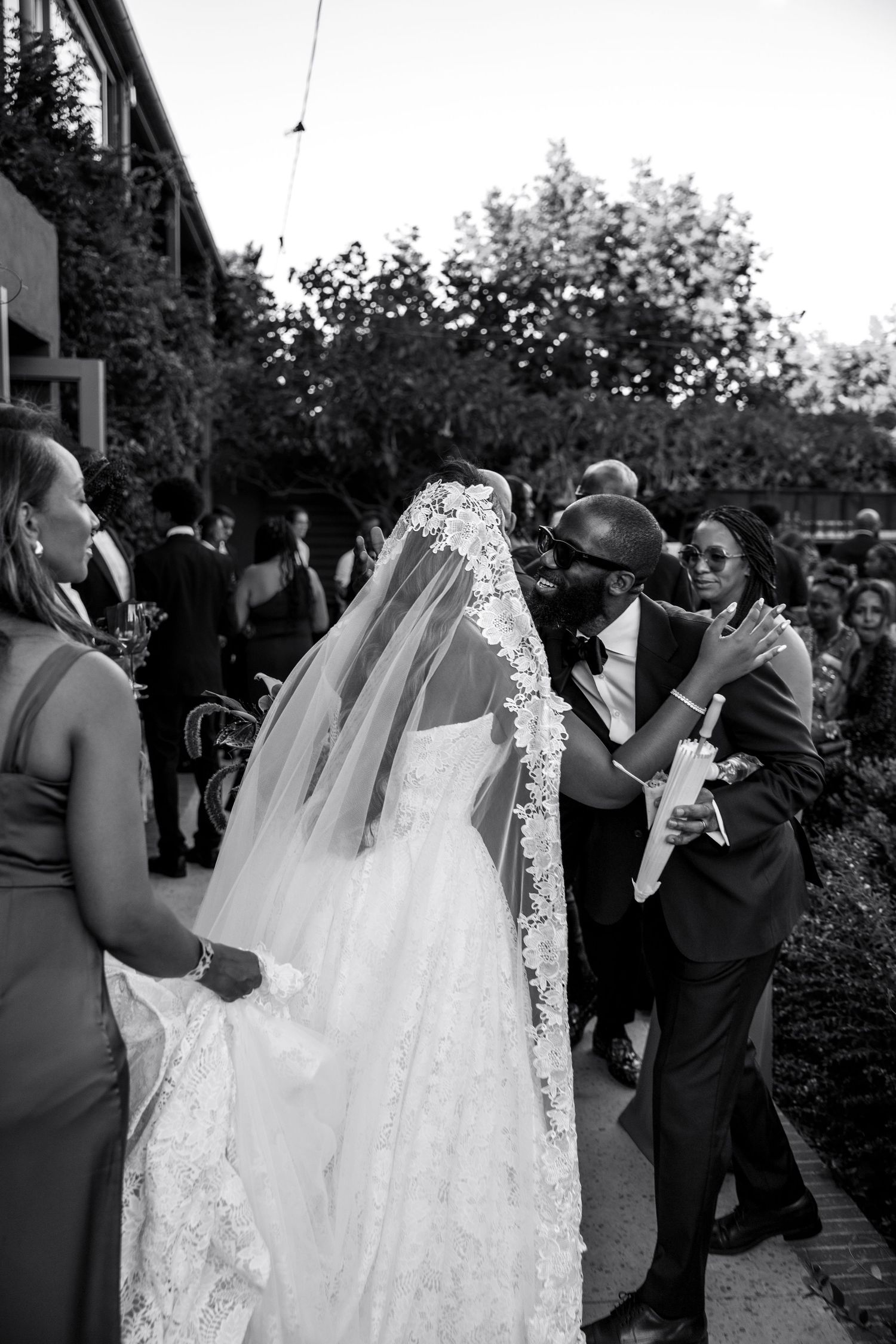 A series of candid black and white wedding photos showing guests and a flowing white bridal gown during an outdoor celebration.
