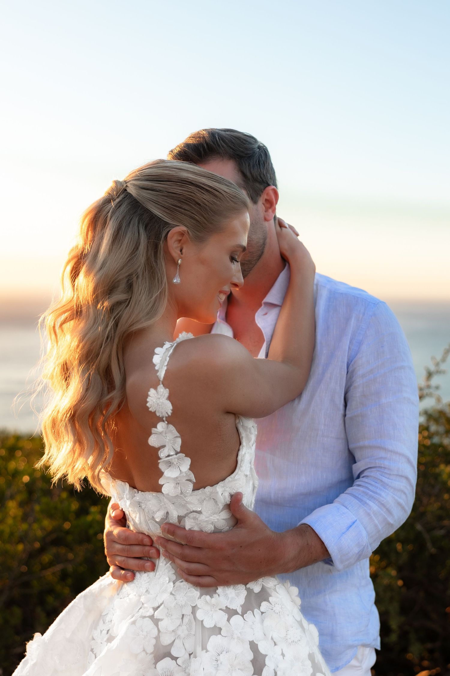 Romantic sunset moment showing couple in wedding attire with bride wearing floral lace dress against golden sky.