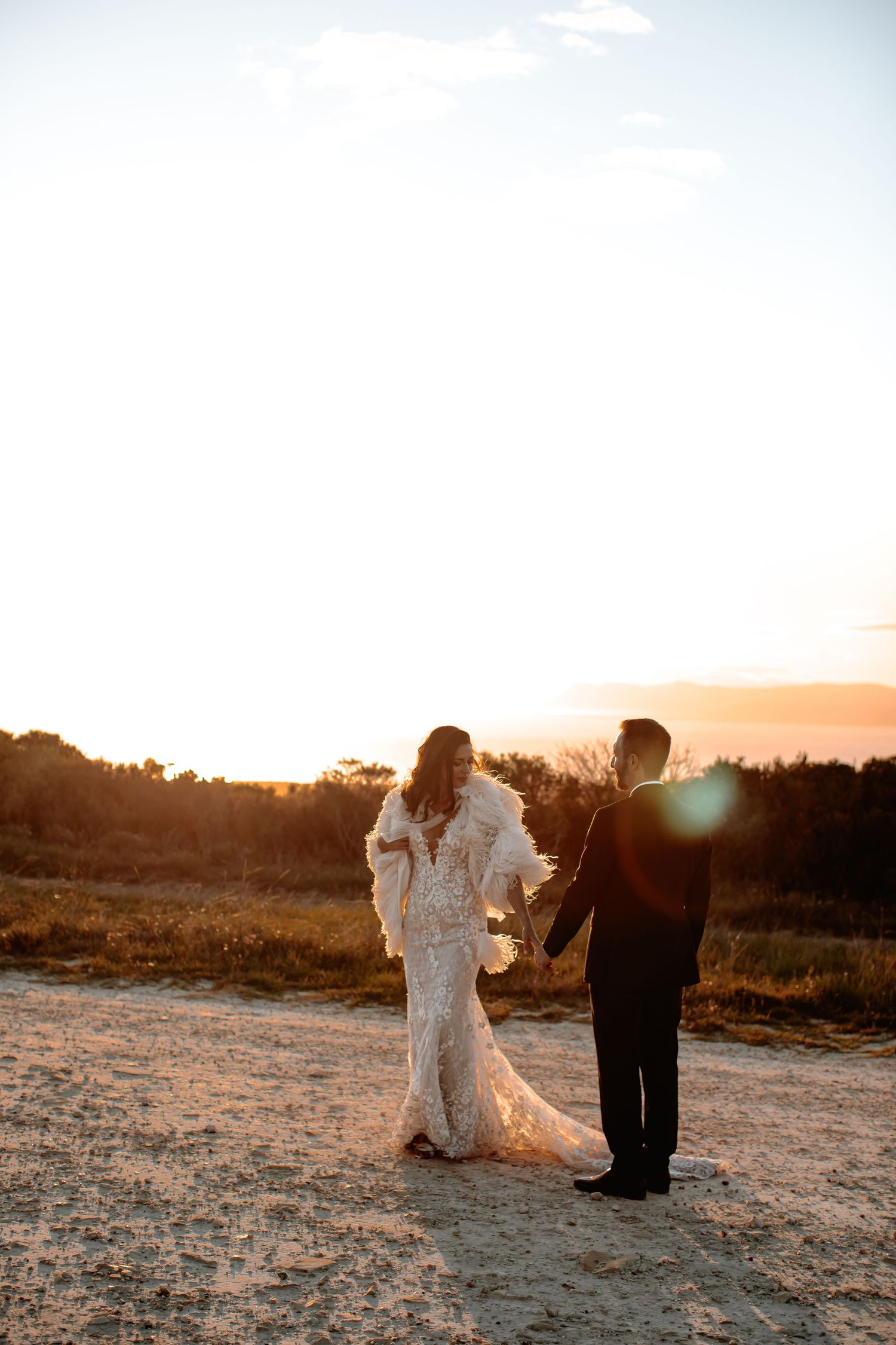 A couple walks hand in hand across a sun-drenched field during golden hour.