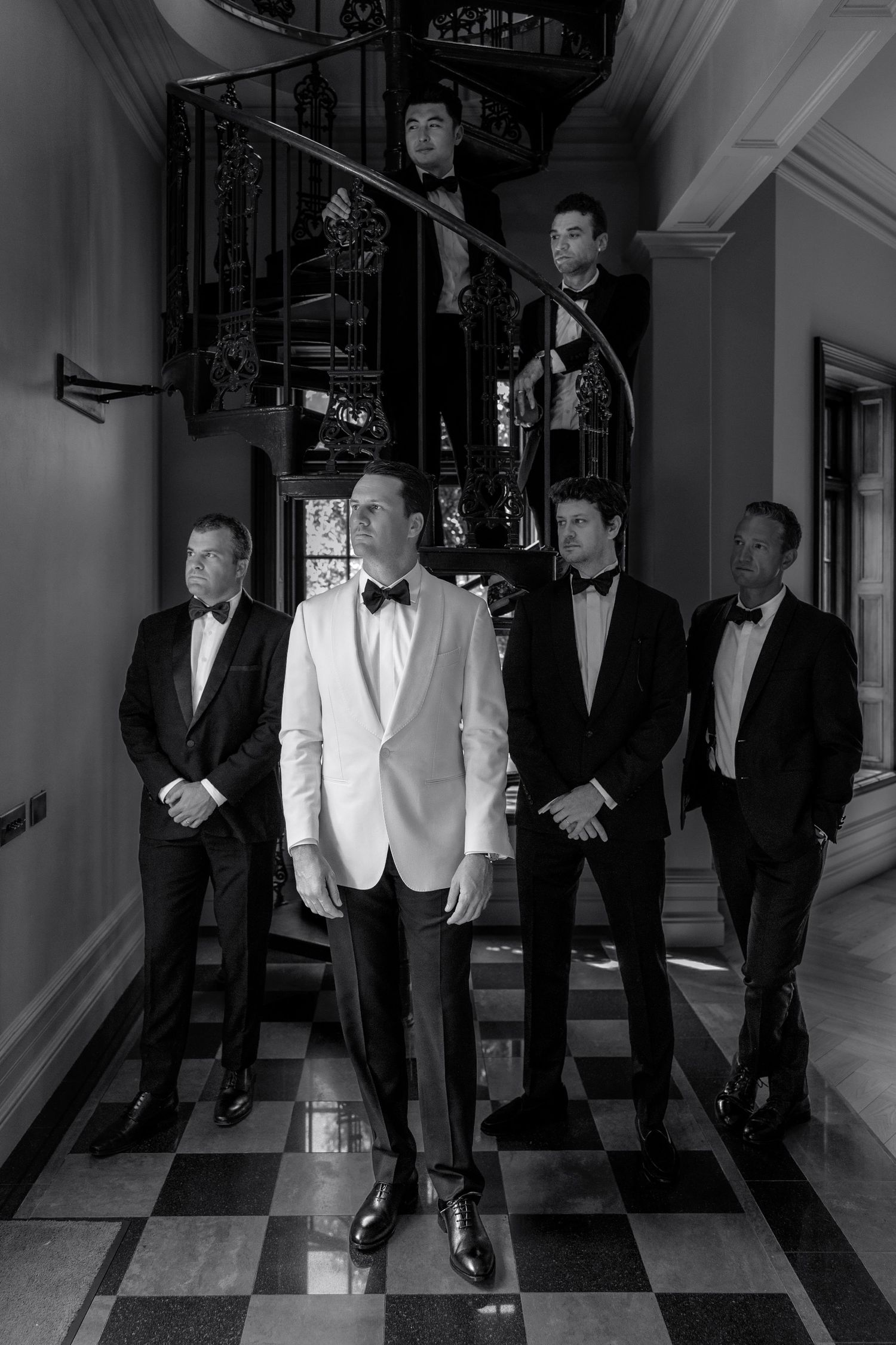A group of men in formal black and white tuxedos walk down an elegant hallway in a stylish fashion.
