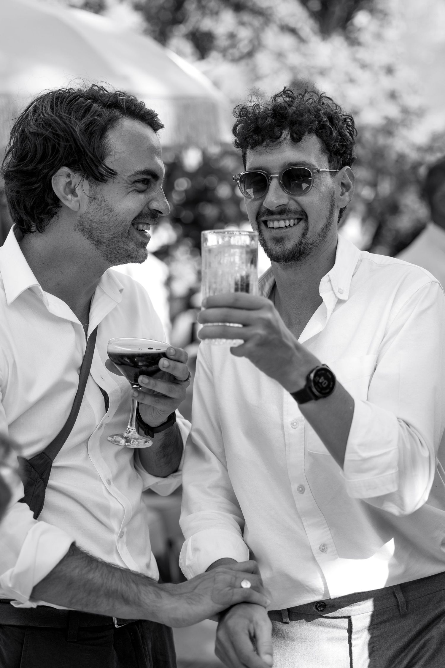 A series of black and white candid photos showing people in white shirts sharing drinks and laughs outdoors.