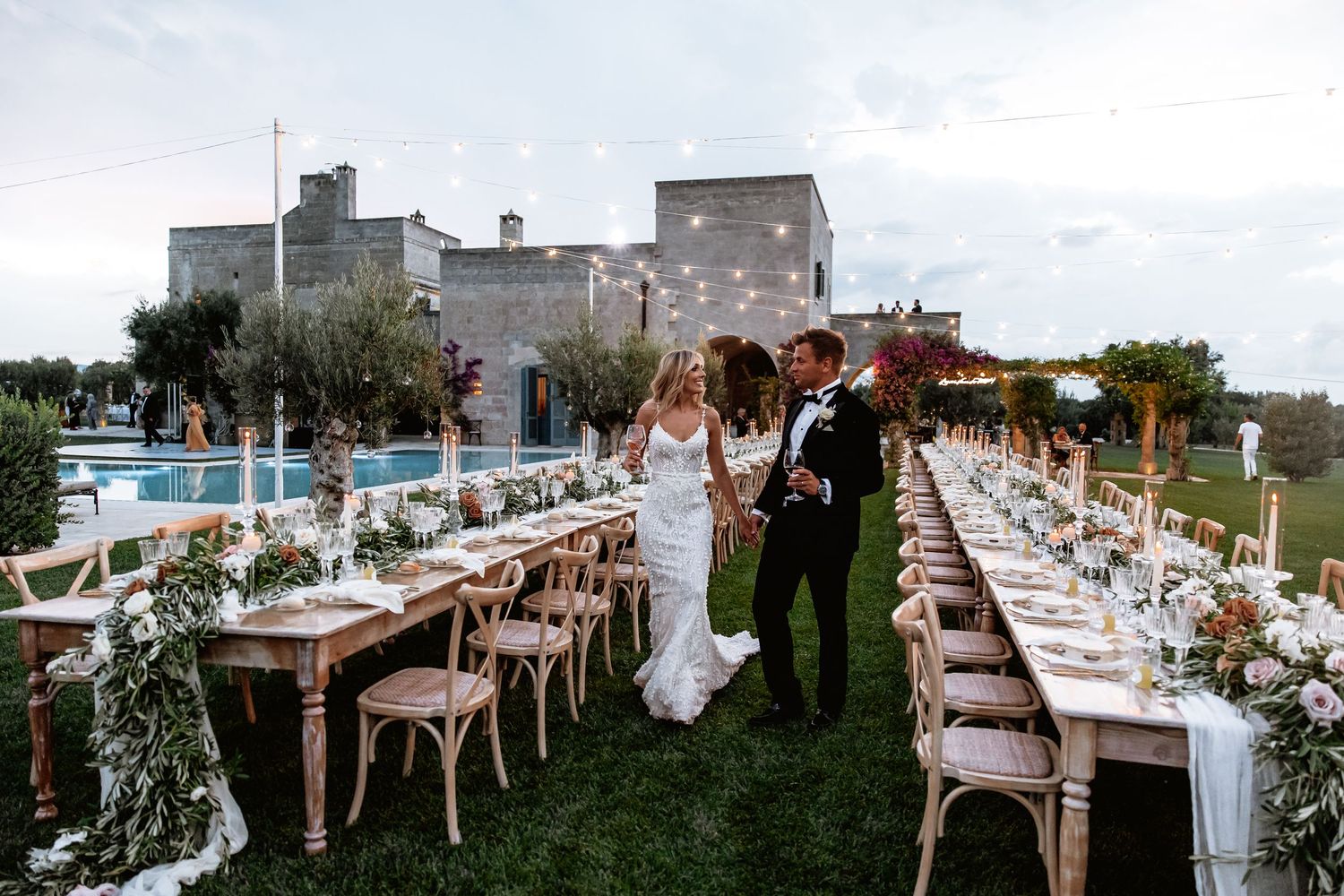 Wedding reception tables decorated with floral centerpieces and white chairs under an open sky.